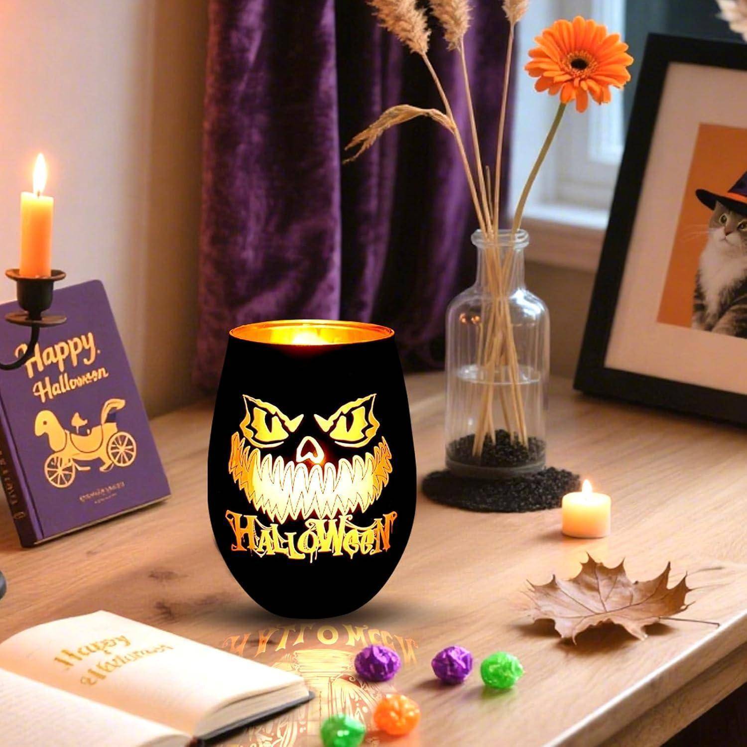Eine Halloween-thematische Tischdekoration mit einer brennenden Kerze, einem kürbisförmigen Glas mit einem grinsenden Gesicht, kleinen Kürbissen, Blättern und einer 'Frohe Halloween' Karte.