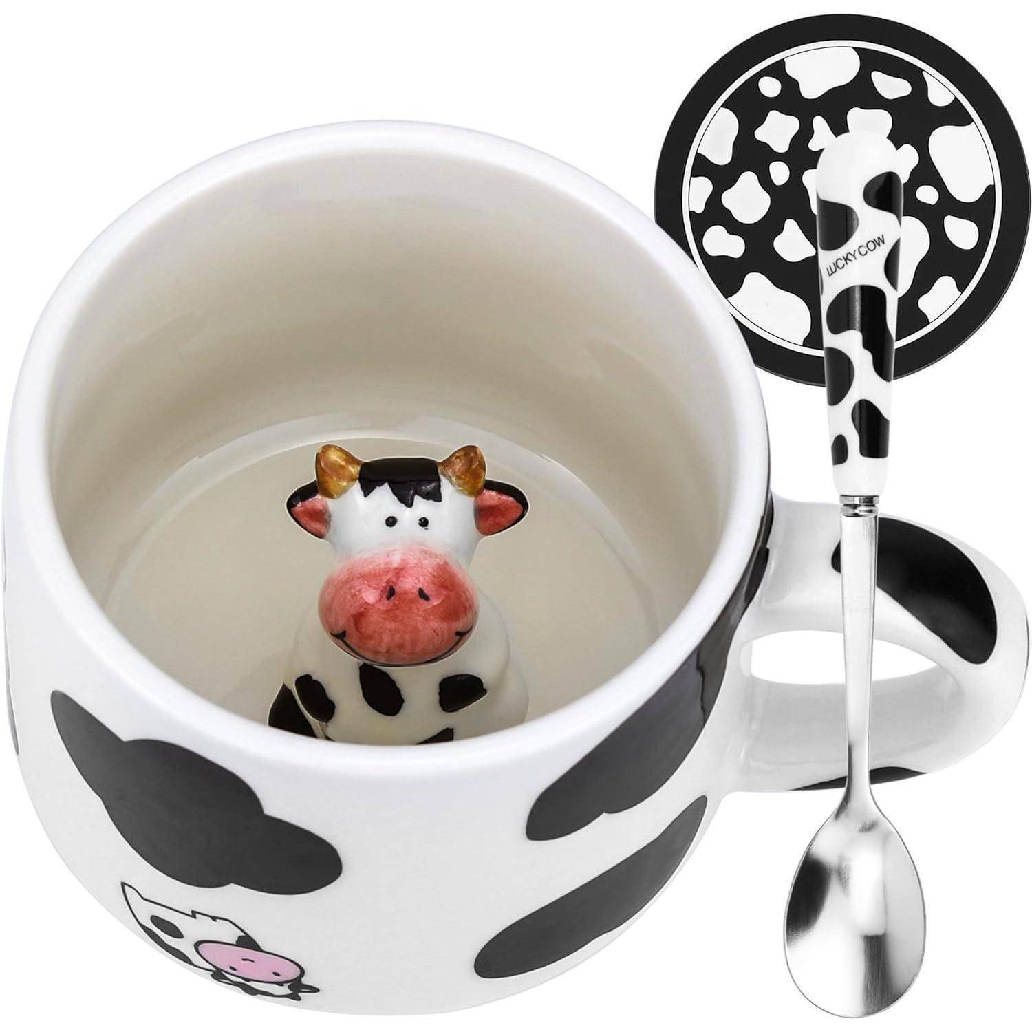 Eine weiße Tasse mit schwarzen Kuhmustern enthält eine keramische Kuhfigur am Boden, versehen mit einem passenden Deckel und Löffel.