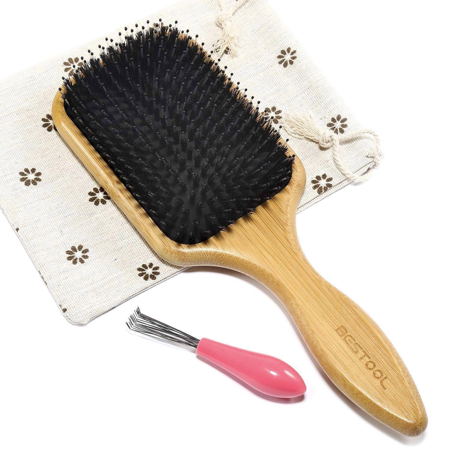 Eine Haarb�rste aus Bambus mit schwarzen Borsten liegt auf einem Stoffbeutel mit Blumenmuster. Ein rosa Reinigungswerkzeug mit Metallborsten befindet sich daneben.
