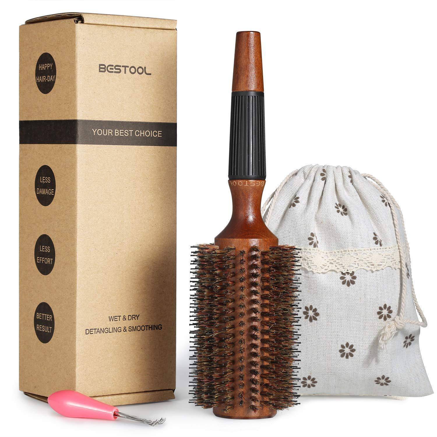 Eine Holzhaarbrürste mit Borsten neben ihrer Verpackungsbox und einem kleinen Stoffbeutel. Ein rosa Werkzeug ist vorne zum Entfernen von Haaren platziert.
