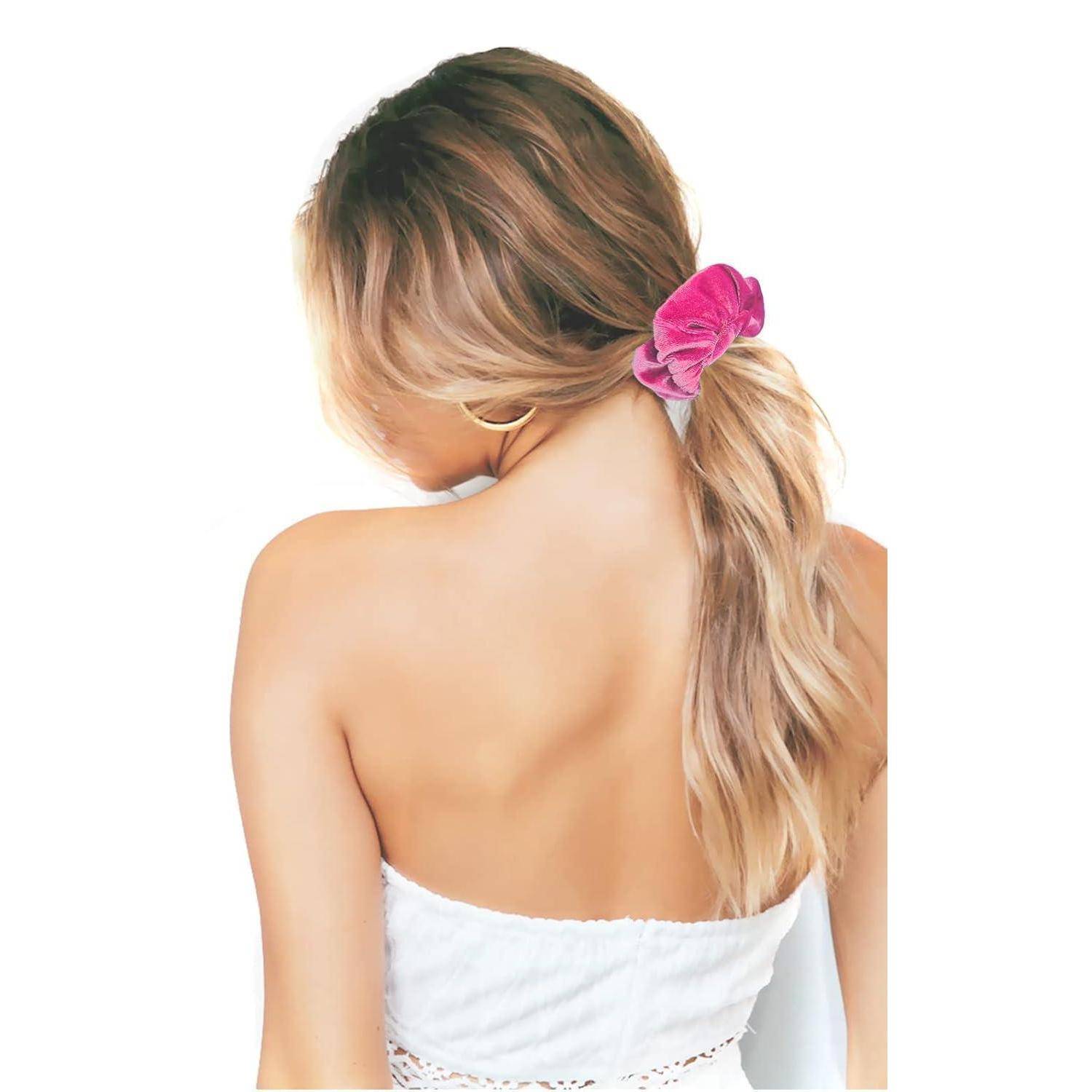 Eine Frau mit langen, welligen Haaren, die einen rosa Haargummi trägt und ein weißes Oberteil anhat, von hinten zu sehen.