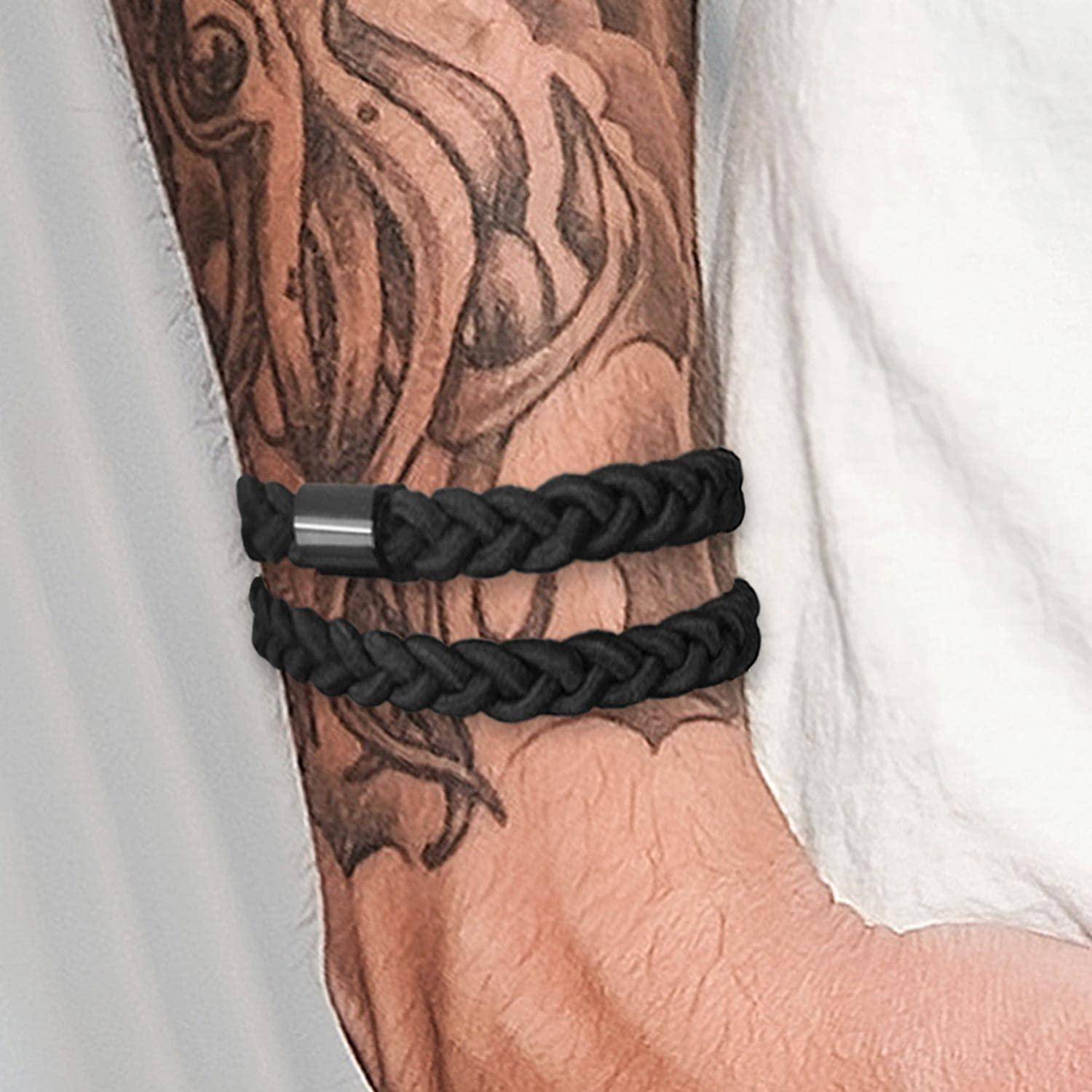 Ein Unterarm mit einem detaillierten Tattoo, das schwarze geflochtene Armbänder zeigt. Das Tattoo präsentiert verspielte Wirbel-Designs auf der Haut.