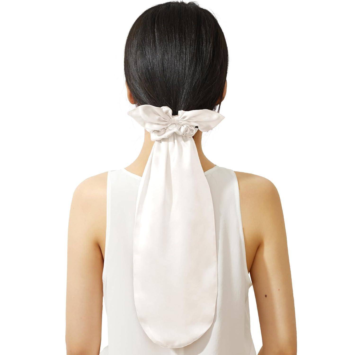 Eine Person mit langen schwarzen Haaren wird von hinten gezeigt, trägt ein weißes Kleidungsstück und eine große, elegante weiße Schleife, die herabfällt.