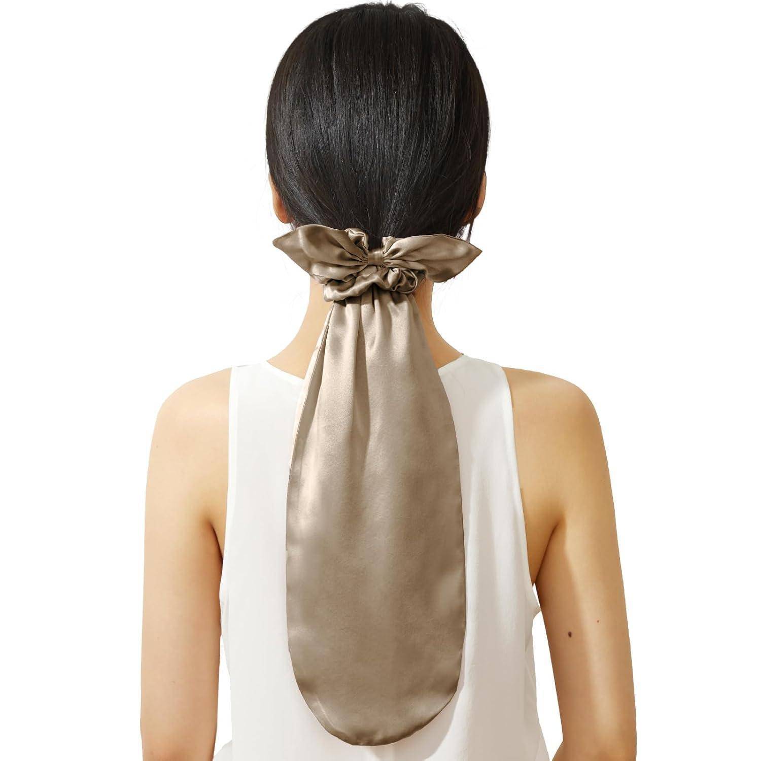 Eine Frau mit langen schwarzen Haaren, die zu einem glatten, niedrigen Zopf gebunden sind und mit einer großen, eleganten Seidenmetallschleife befestigt werden.