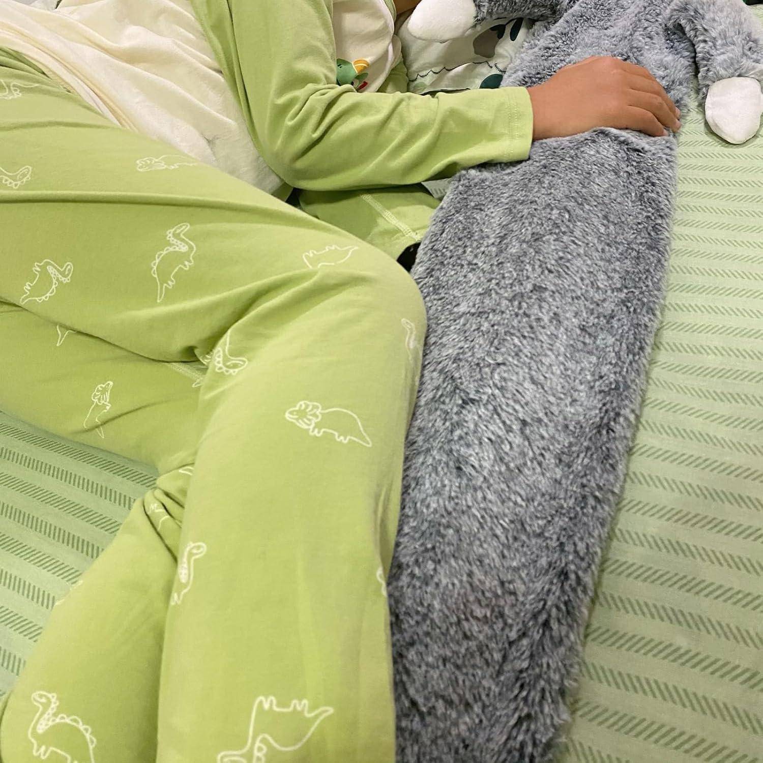 Kind in grünem Schlafanzug mit Dinosaurier-Muster kuschelt ein langes, flauschiges Stofftier im Bett. Die Umgebung ist gemütlich und ruhig.