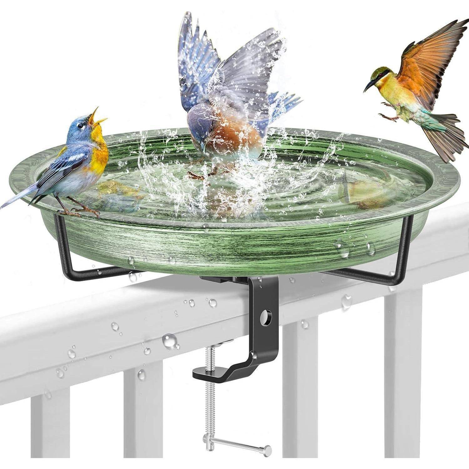 Ein grünes Vogelbad mit zwei bunten Vögeln, die im Wasser spielen und einem weiteren, der in der Nähe landet, befestigt an einem weißen Geländer mittels einer Metallhalterung.