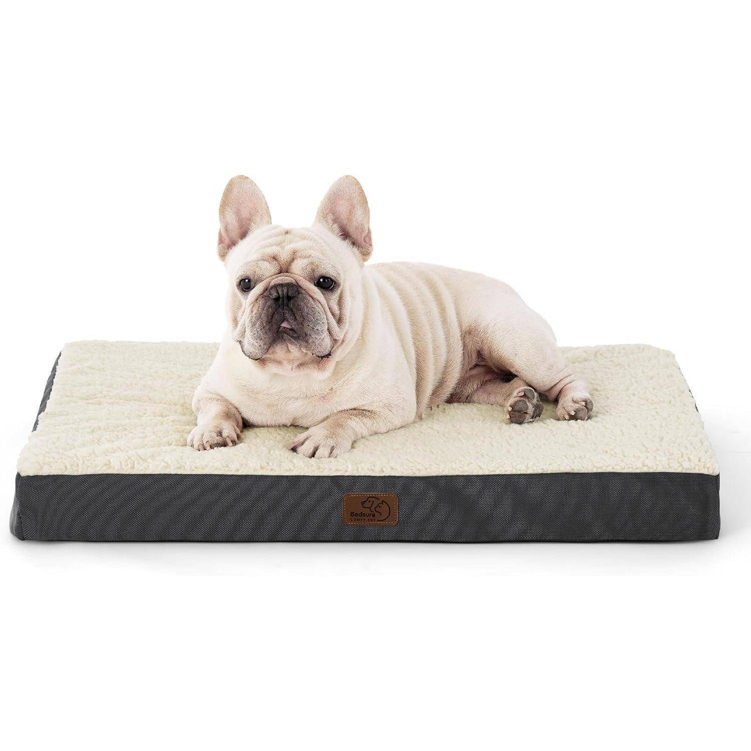 Ein French Bulldog, der auf einem beigen Hundebett mit gepolsterter Oberfläche liegt und in die Kamera blickt. Das Bett hat eine schwarze Basis und ein kleines Logo.