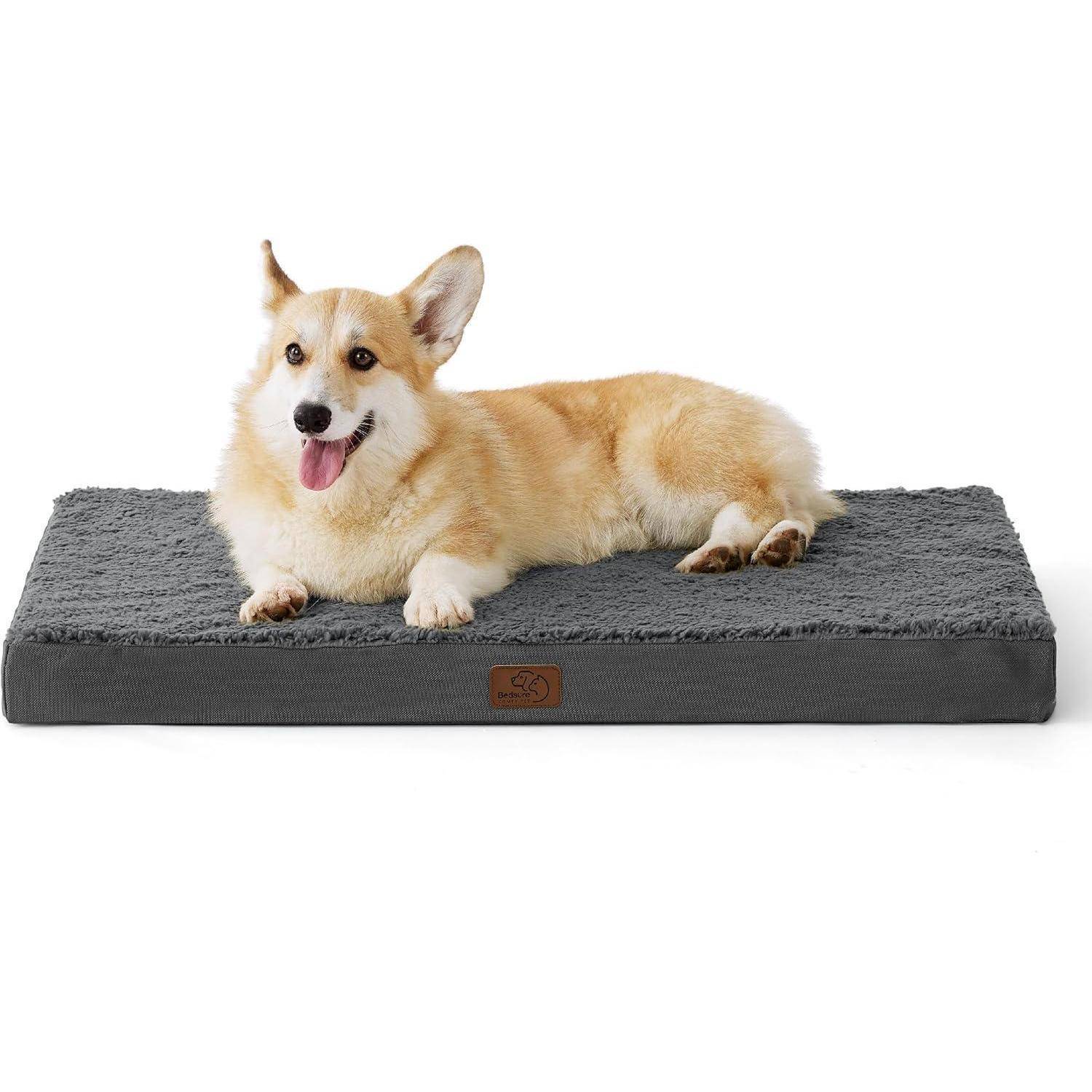 „Ein Corgi liegt auf einem weichen, grauen rechteckigen Hundebett und sieht zufrieden aus, mit heraushängender Zunge.