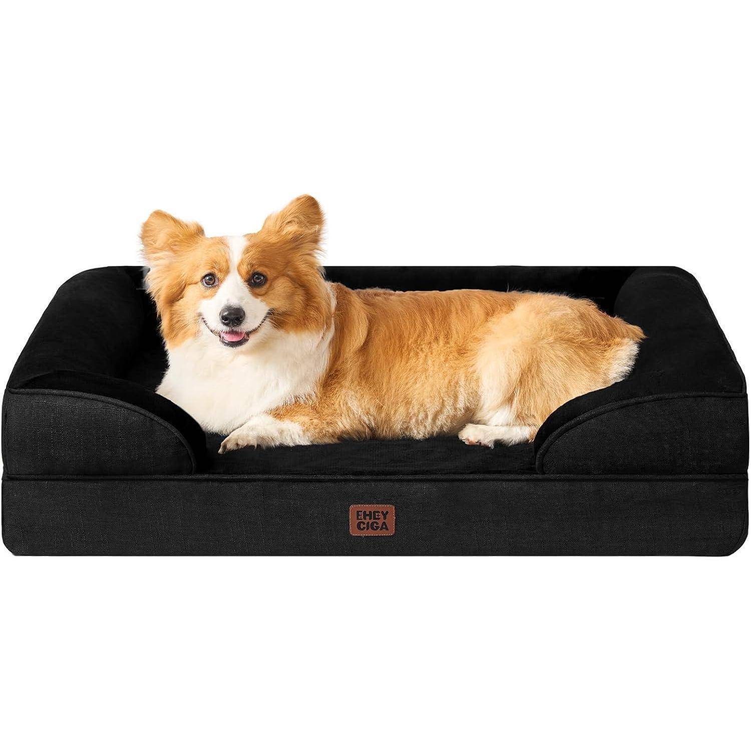 Ein kleiner brauner und weißer Hund sitzt gemütlich auf einem schwarzen Plüsch-Haustierbett und blickt mit einem fröhlichen Ausdruck in die Kamera.