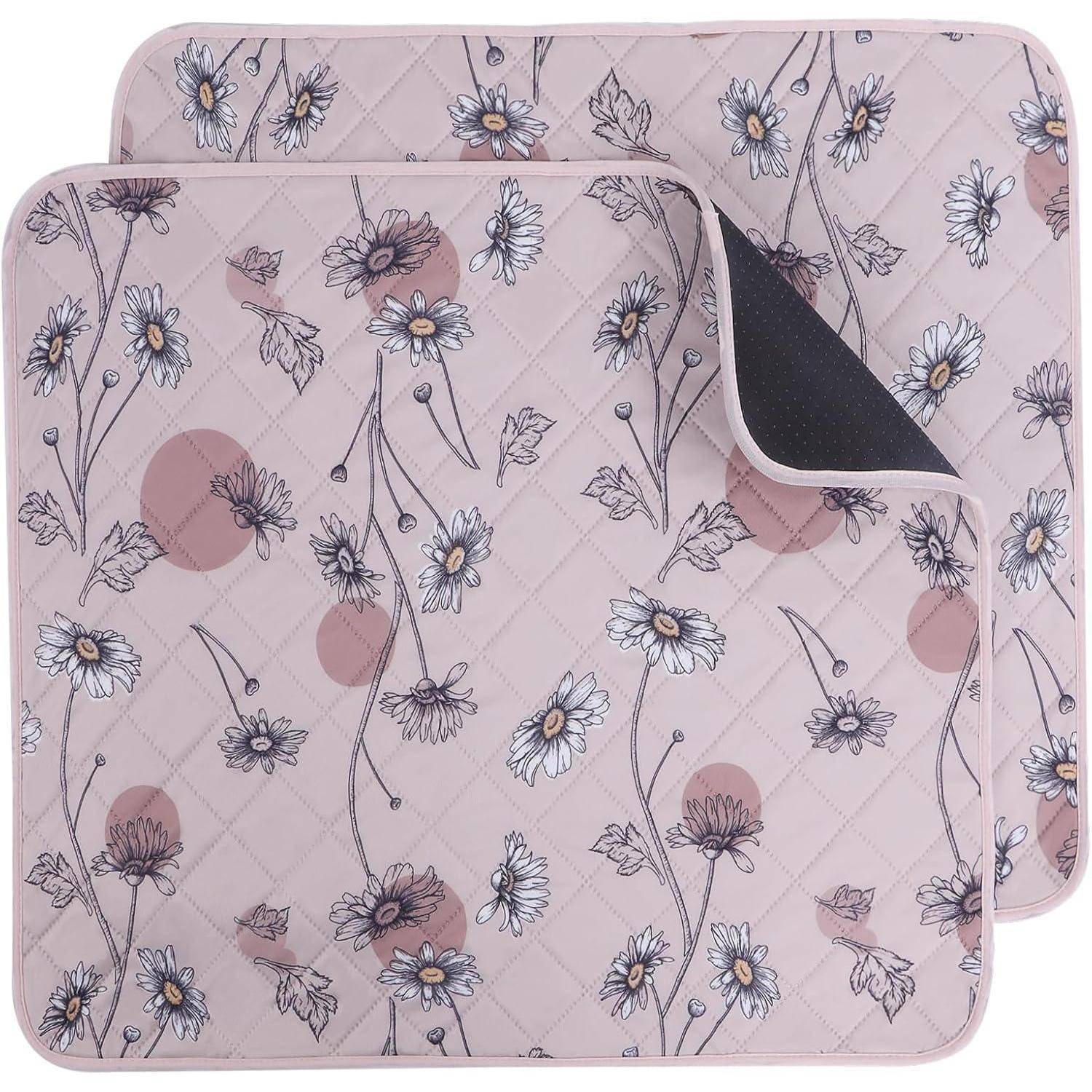 Zwei gesteppte, quadratische rosa Matten mit Blumen- und Kreismustern. Die obere Matte ist leicht gefaltet, um die schwarze Rückseite zu zeigen.