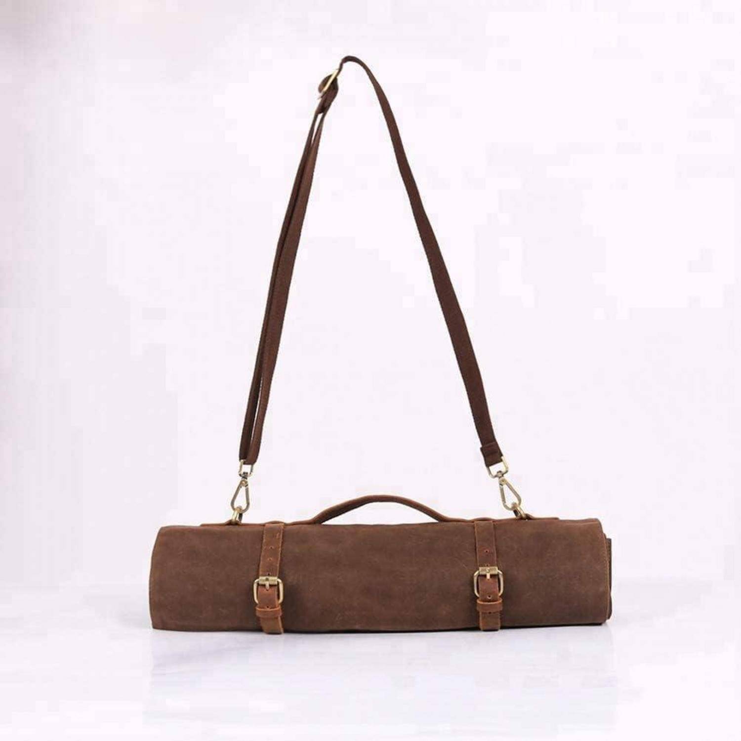 Eine braune Ledertasche mit Schulterriemen und zwei Schnallen, die auf einer weißen Oberfläche liegt.
