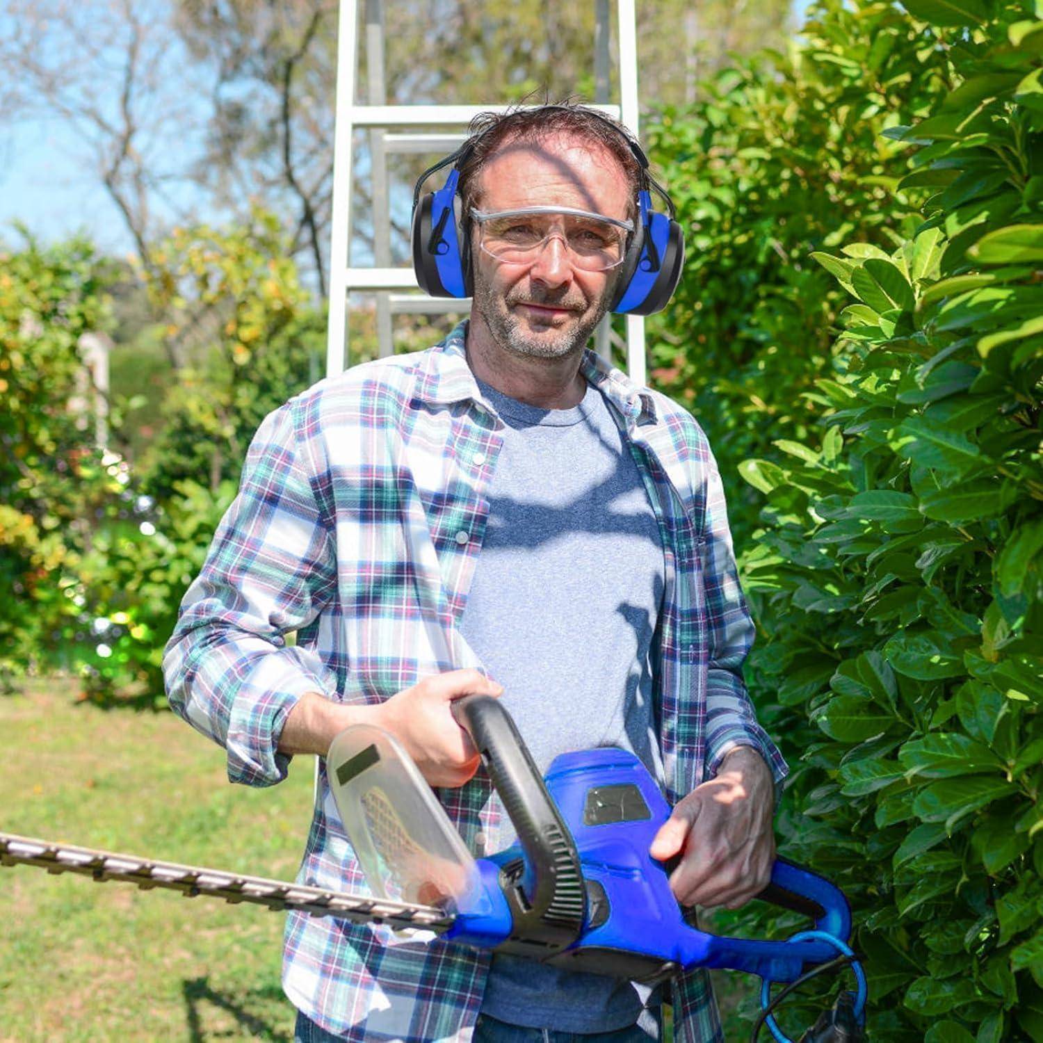 Ein Mann mit Schutzausrüstung verwendet einen elektrischen Heckenschneider an einem Strauch in einem Garten, wobei eine Leiter im Hintergrund sichtbar ist.