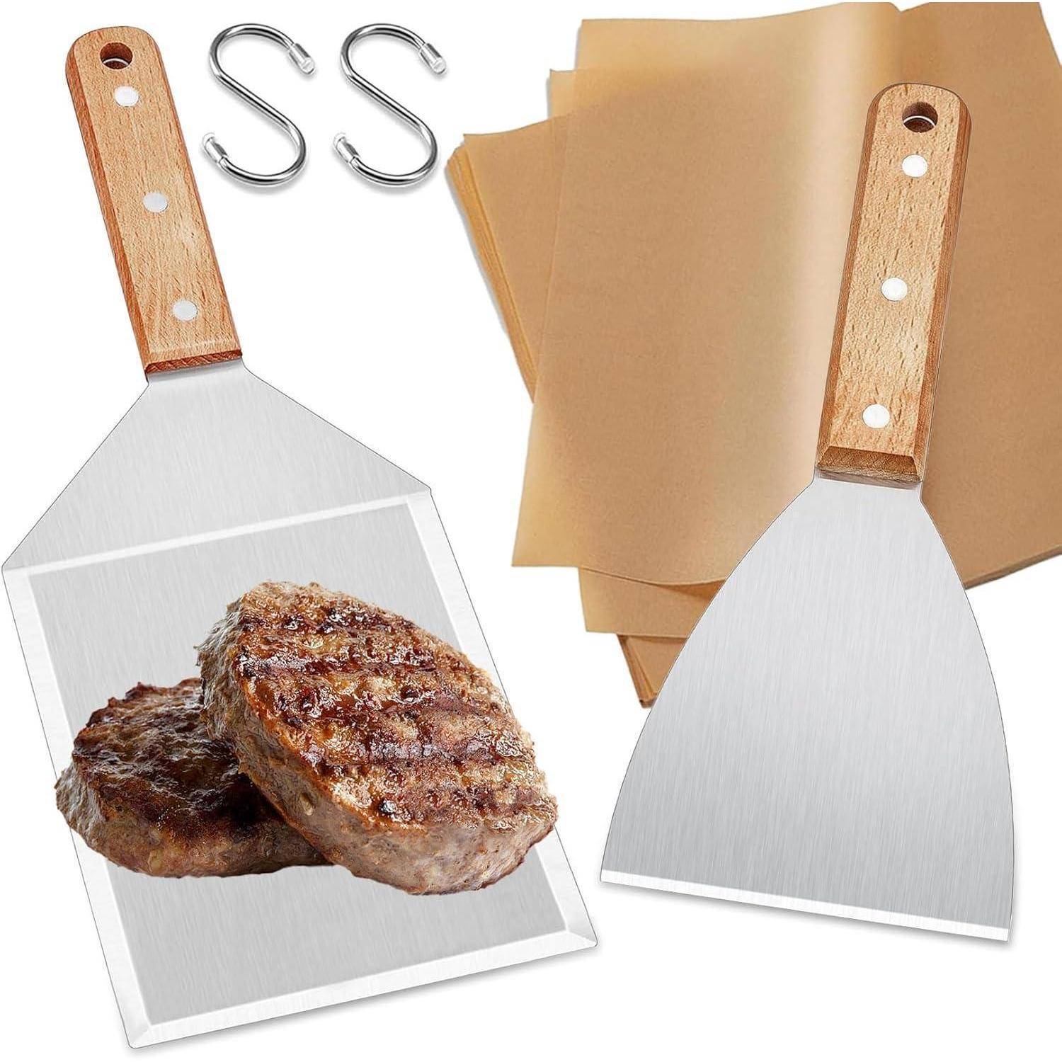 Zwei Metallspatel mit Holzgriffen, Backpapierbögen und 'S'-förmigen Haken neben gekochten Fleischpuffern auf einem Tisch.