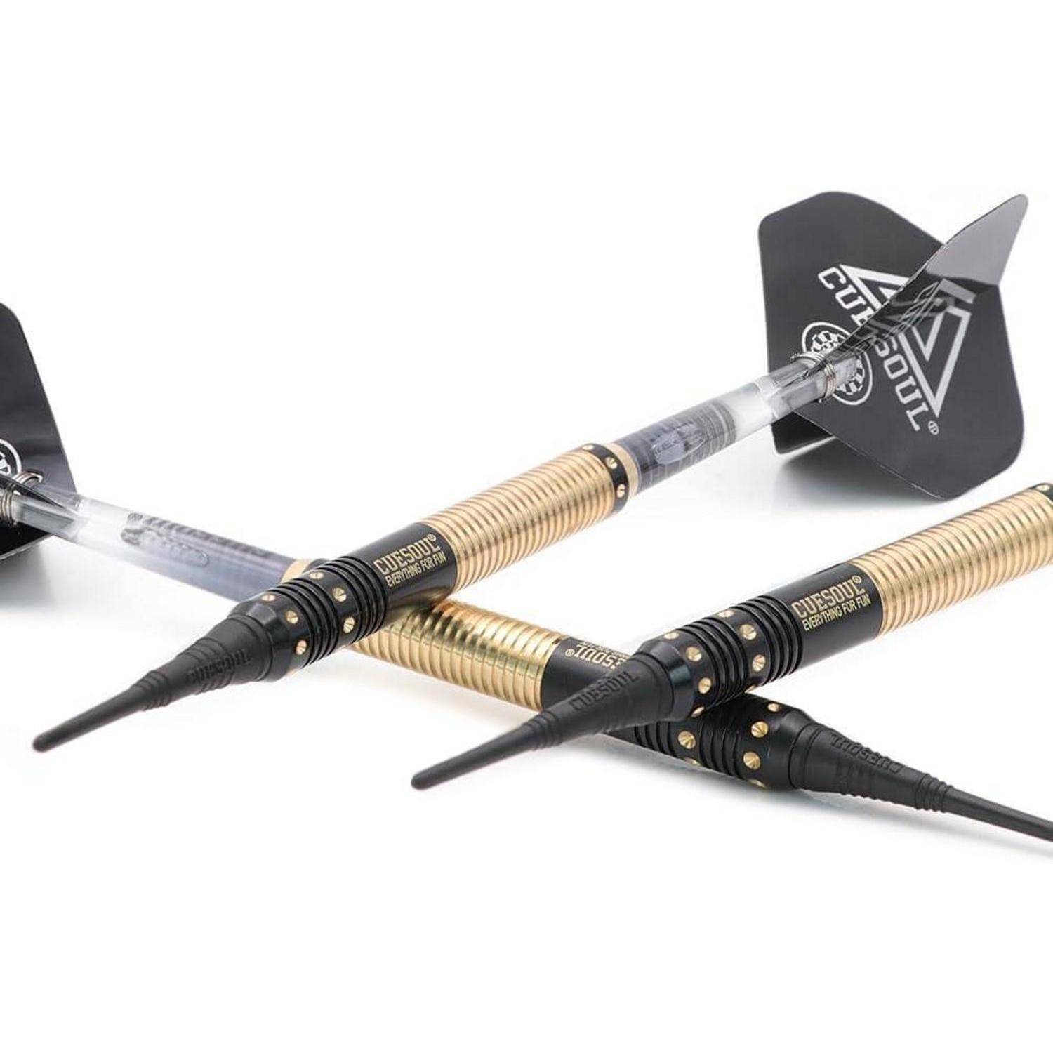 Zwei metallische Dartpfeile mit schwarz-goldenen Details und Flügeln mit geometrischem Muster liegen gekreuzt auf einer weißen Oberfläche.