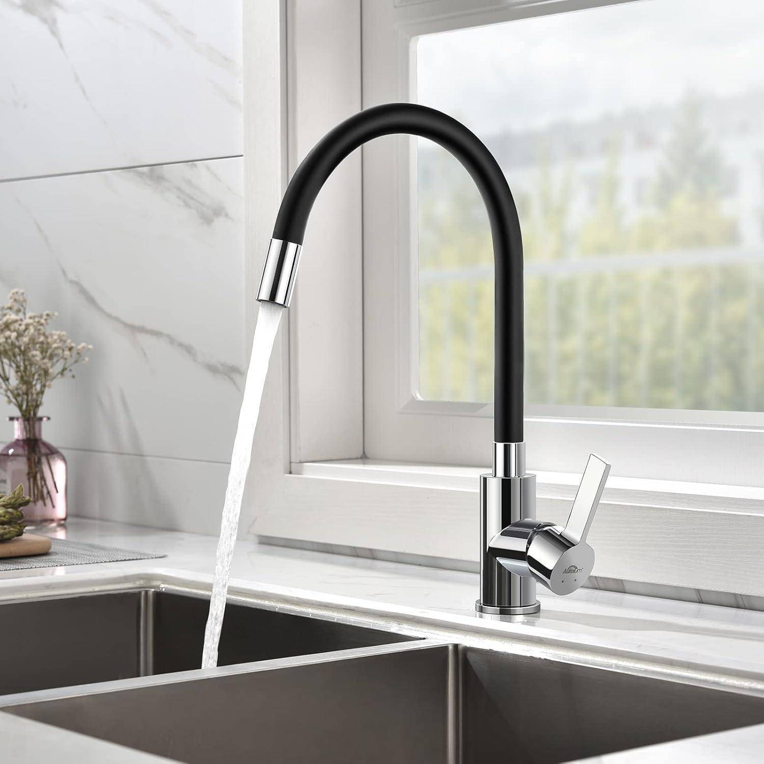 Ein moderner Küchenspülstein mit einem schwarzen geschwungenen Wasserhahn lässt Wasser in ein Edelstahlbecken fließen, vor einem weißen Fliesenspiegel und einem Fenster.