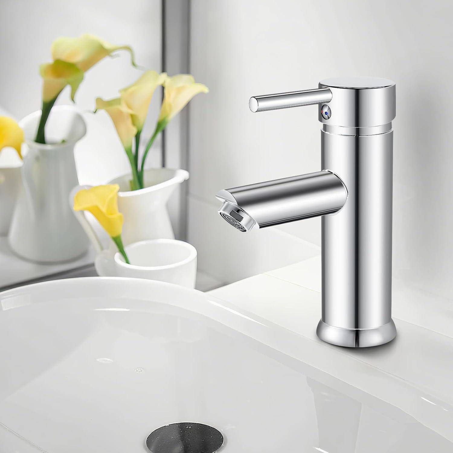 Ein moderner Chrom-Wasserhahn ist über einem weißen Waschbecken installiert. Im Hintergrund befinden sich weiße Vasen mit gelben Blumen.