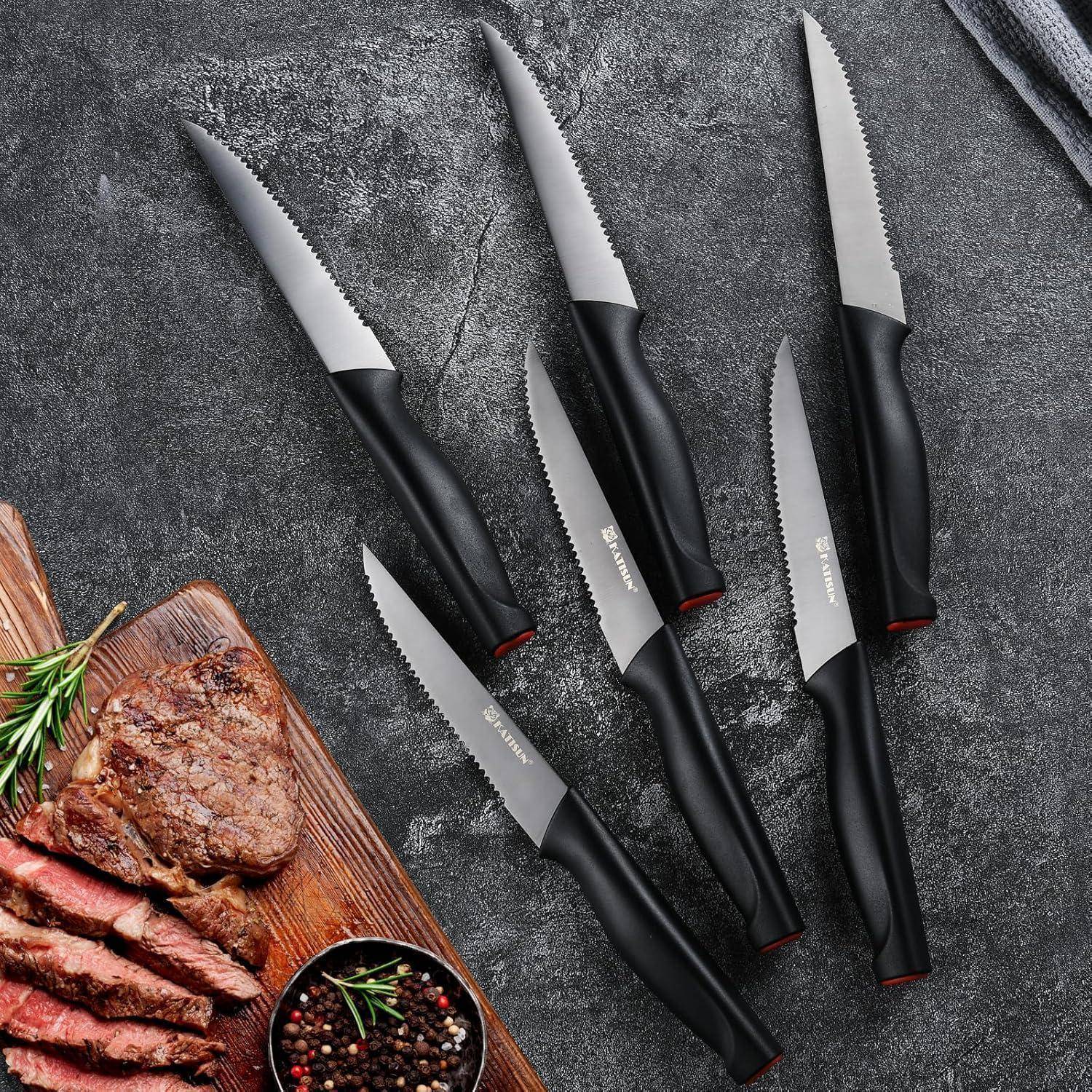 Sechs gezahnte Messer mit schwarzen Griffen sind diagonal auf einer grauen Steinoberfläche neben einem Holzbrett mit geschnittenem Steak und Kräutern angeordnet.