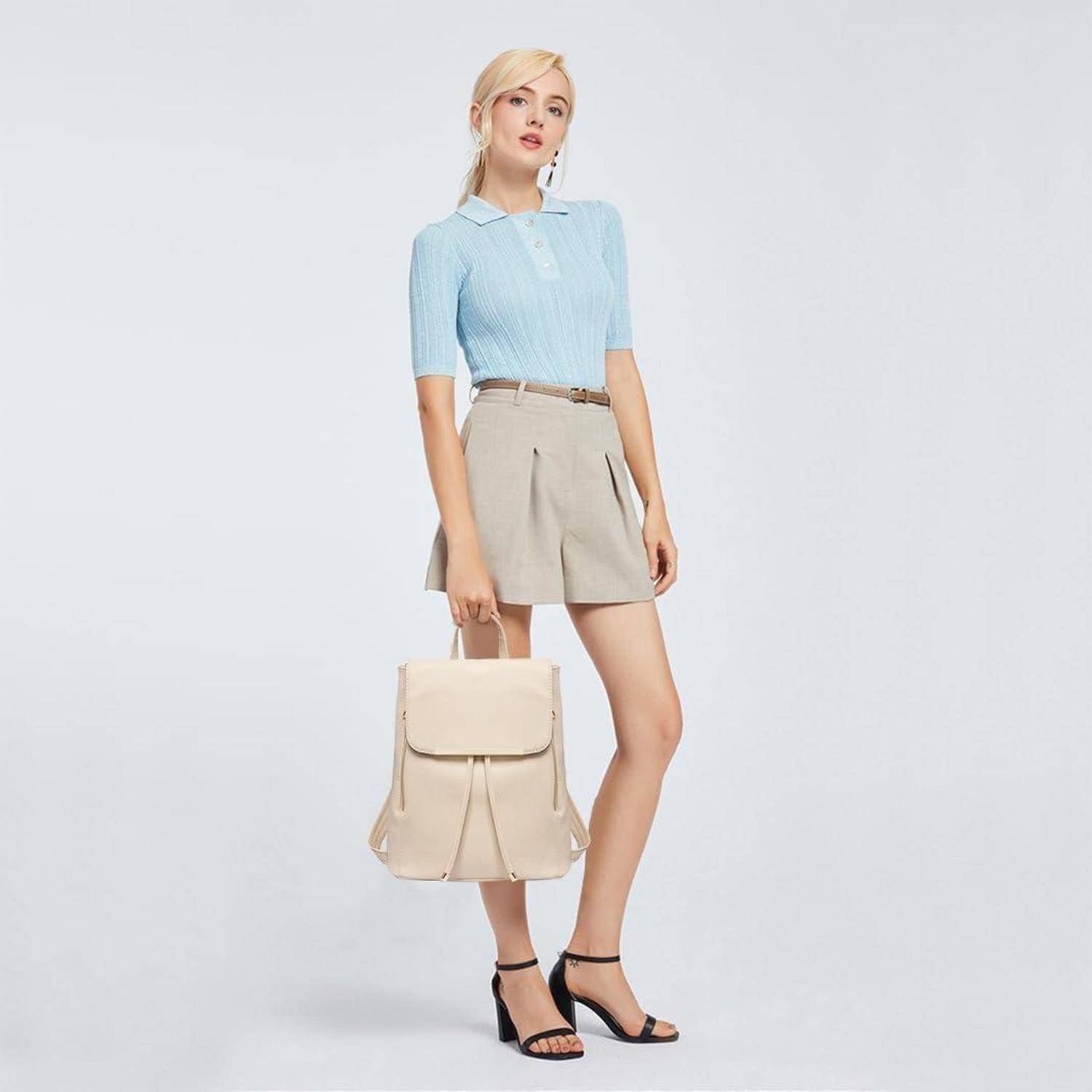 Eine Person in einem hellblauen Hemd und einem beigen Rock, die einen beigen Rucksack trägt, steht vor einem einfarbigen Hintergrund und präsentiert einen lässigen Outfit.