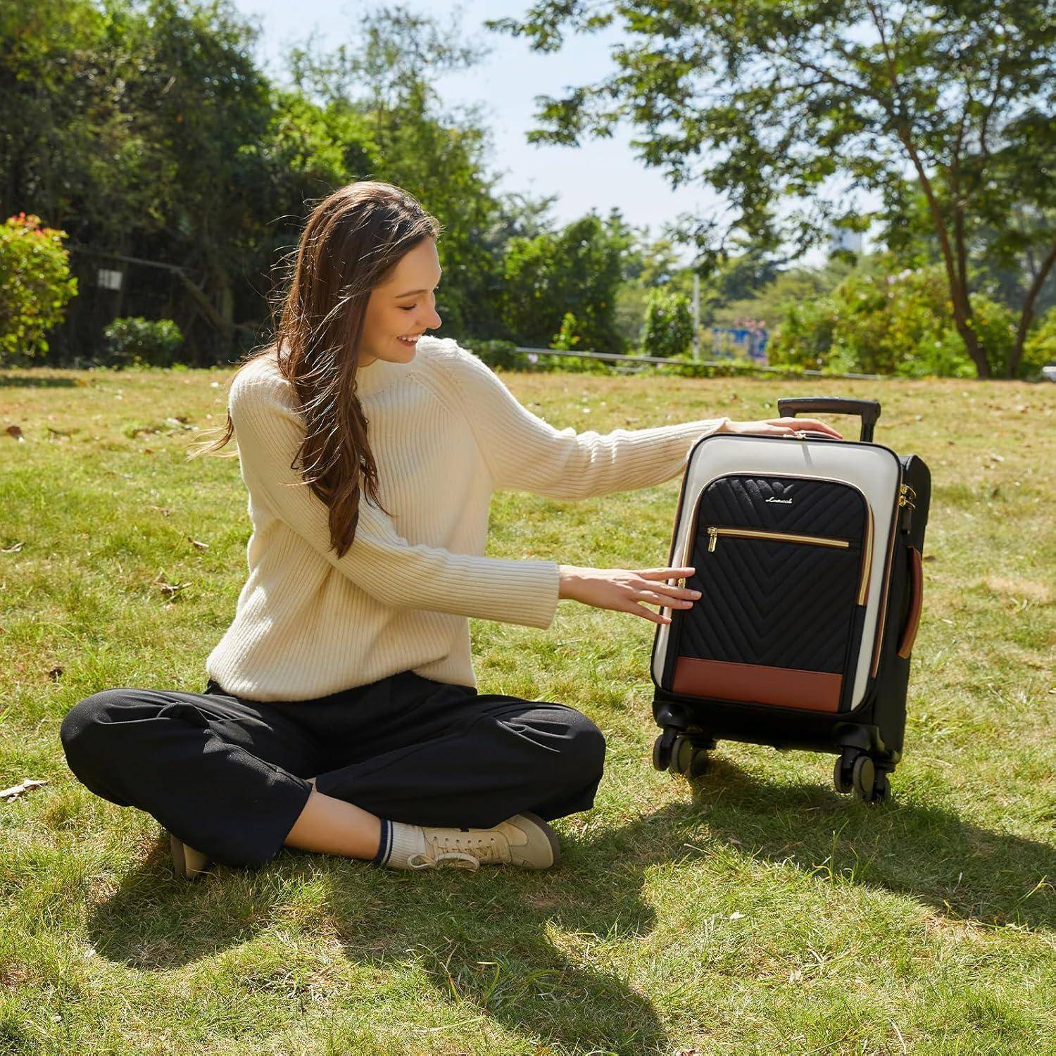 Eine Frau sitzt auf dem Gras, lächelt und streckt die Hand nach einem schwarzen Koffer mit braunen Akzenten aus. Sie trägt lässige Kleidung. Bäume und Sonnenlicht im Hintergrund.
