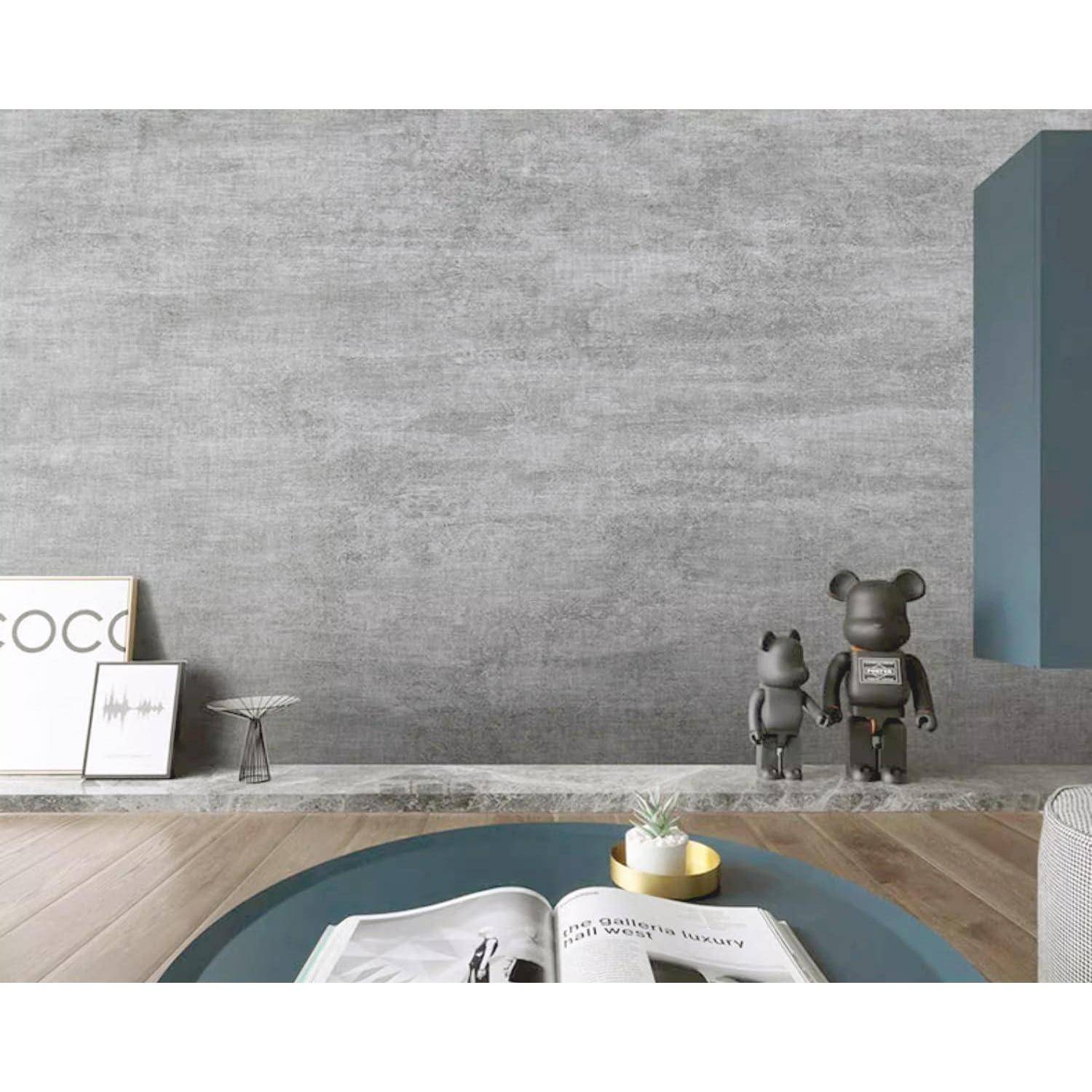 Ein modernes Wohnzimmer mit einer strukturierten grauen Wand, Holzboden, kleinen Skulpturen und einem runden Couchtisch mit einem Buch und einer Kerze.
