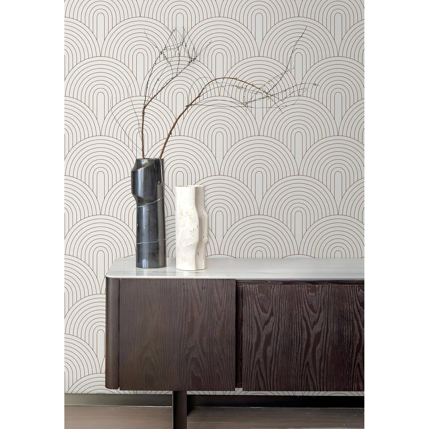 Eine minimalistische Vasenanordnung mit dünnen Ästen auf einem Holzsideboard vor einer geometrisch gemusterten Tapete.
