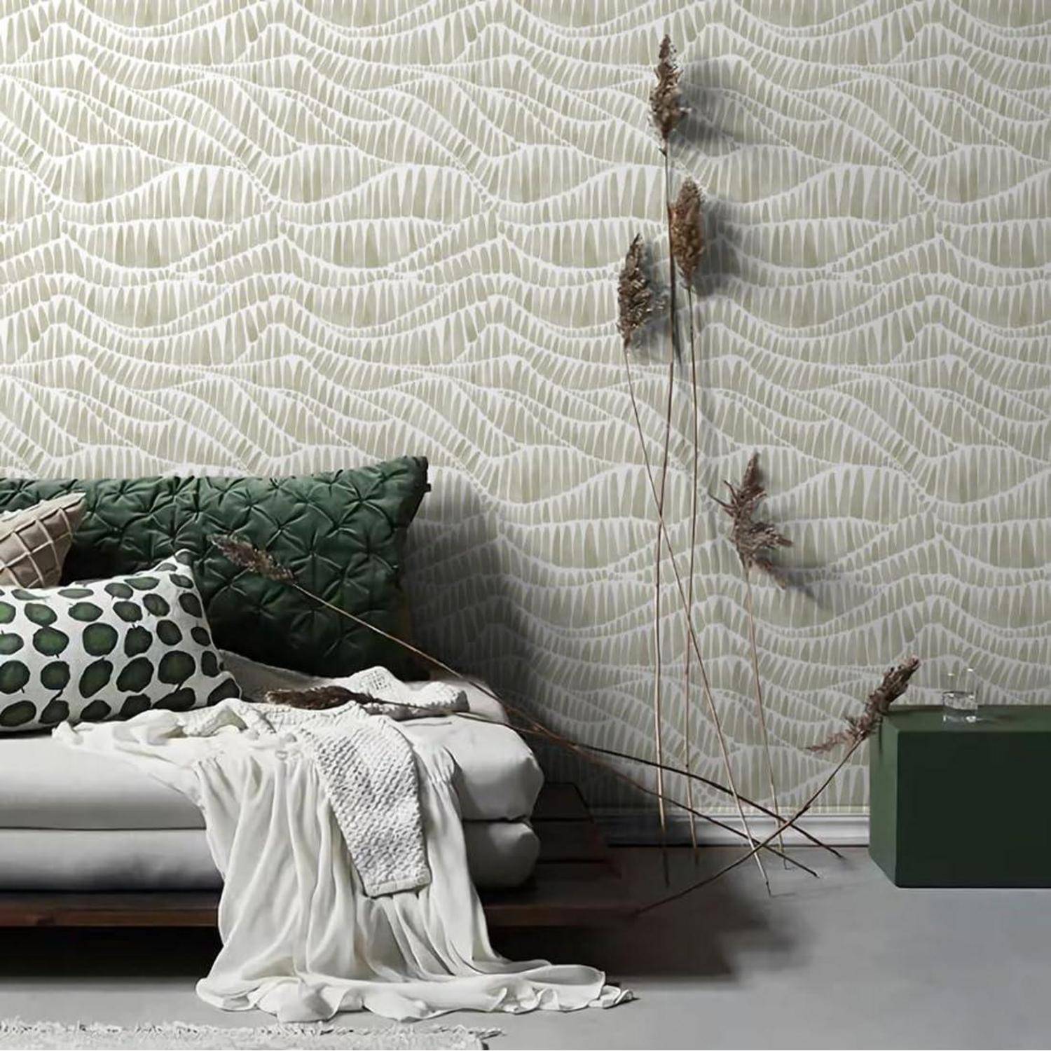 Ein moderner Wohnraum zeigt ein weißes Sofa mit grünen und gemusterten Kissen. Eine strukturierte, wellenförmig gemusterte Wand und hohe Schilfrohre verleihen Eleganz.