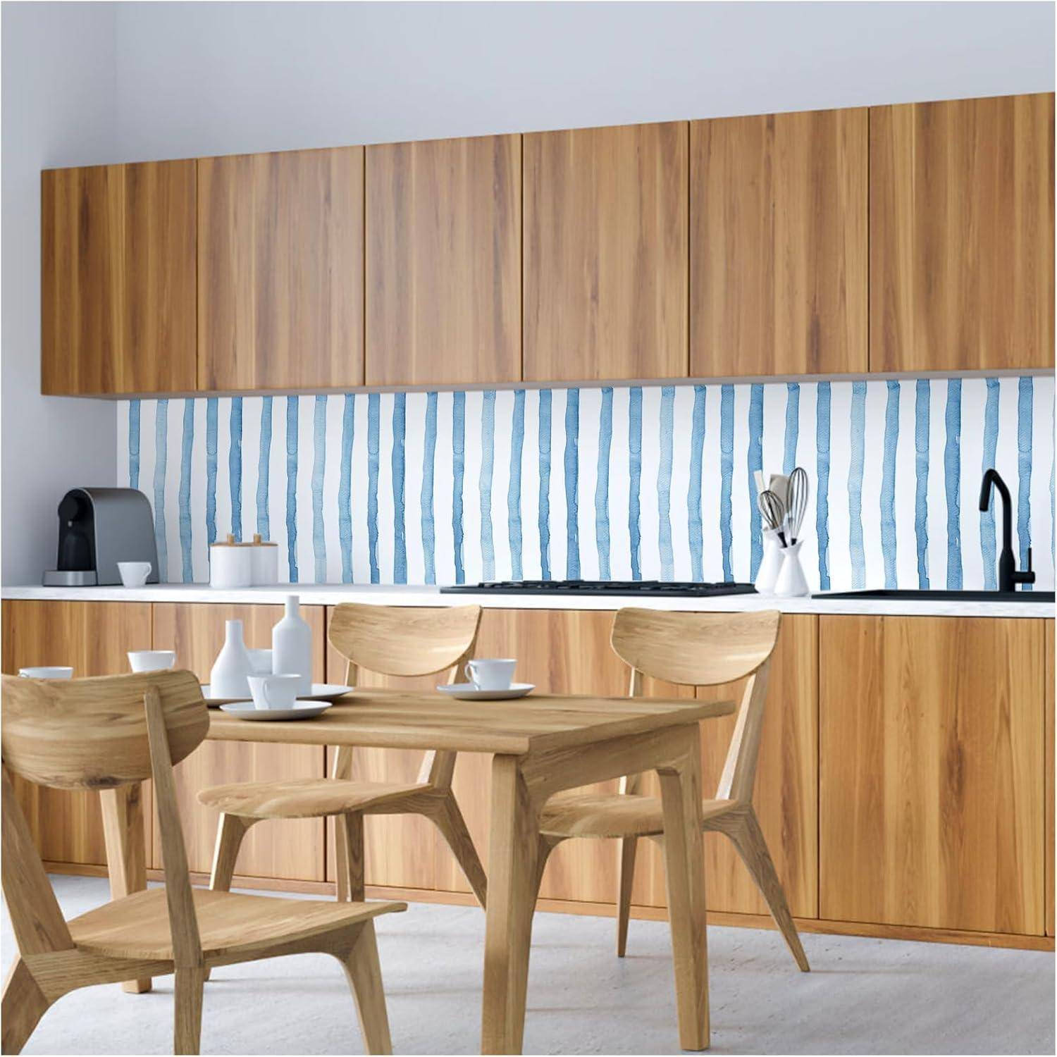 Küche mit Holzschränken, einer Kaffeemaschine und einem gestreiften blau-weißen Fliesenspiegel. Ein Tisch und Stühle befinden sich im Vordergrund.