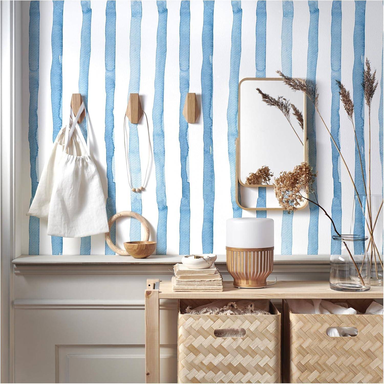 Eine dekorative Wand mit vertikalen blauen Streifen ziert Accessoires, einen Spiegel und getrocknete Pflanzen. Darunter sind geflochtene Körbe auf einem Regal platziert.