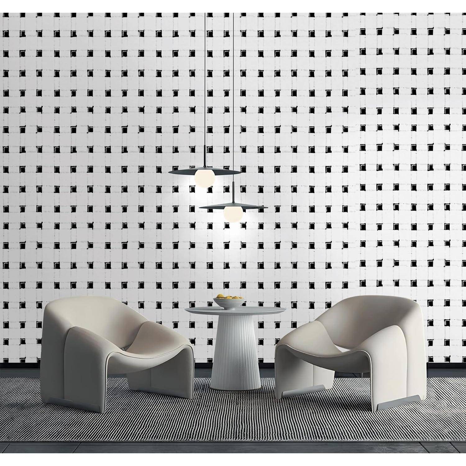 Zwei moderne Stühle stehen einer kleinen runden Tisch mit einem Mittelstück auf einem gemusterten Teppich gegenüber, vor einer gitternetzförmig gemusterten Wand mit Pendelleuchten darüber.