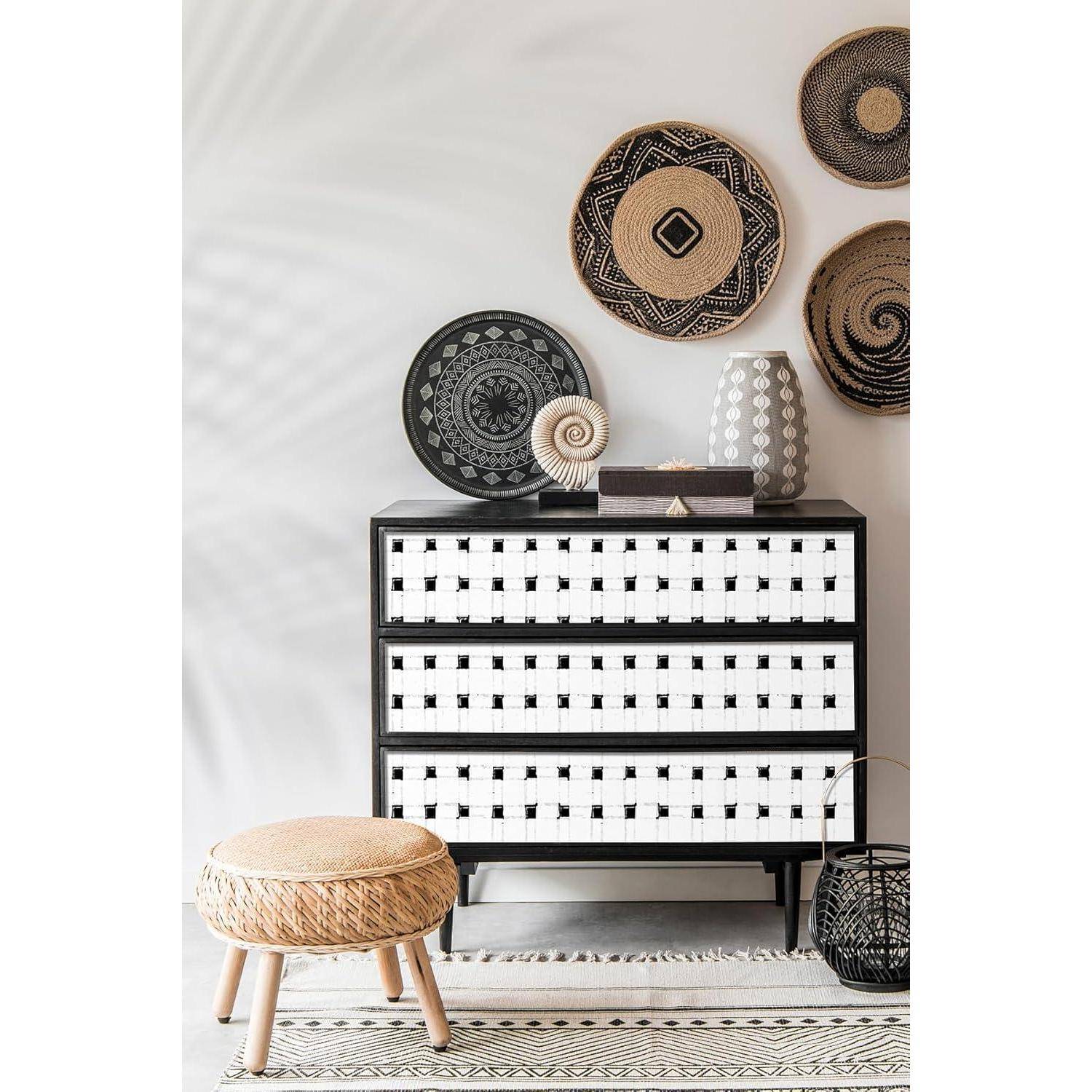 Ein schwarz-weißes kariertes Sideboard mit Vasen und dekorativen Gegenständen oben drauf, Körben an der Wand und einem runden Hocker auf einem gemusterten Teppich.