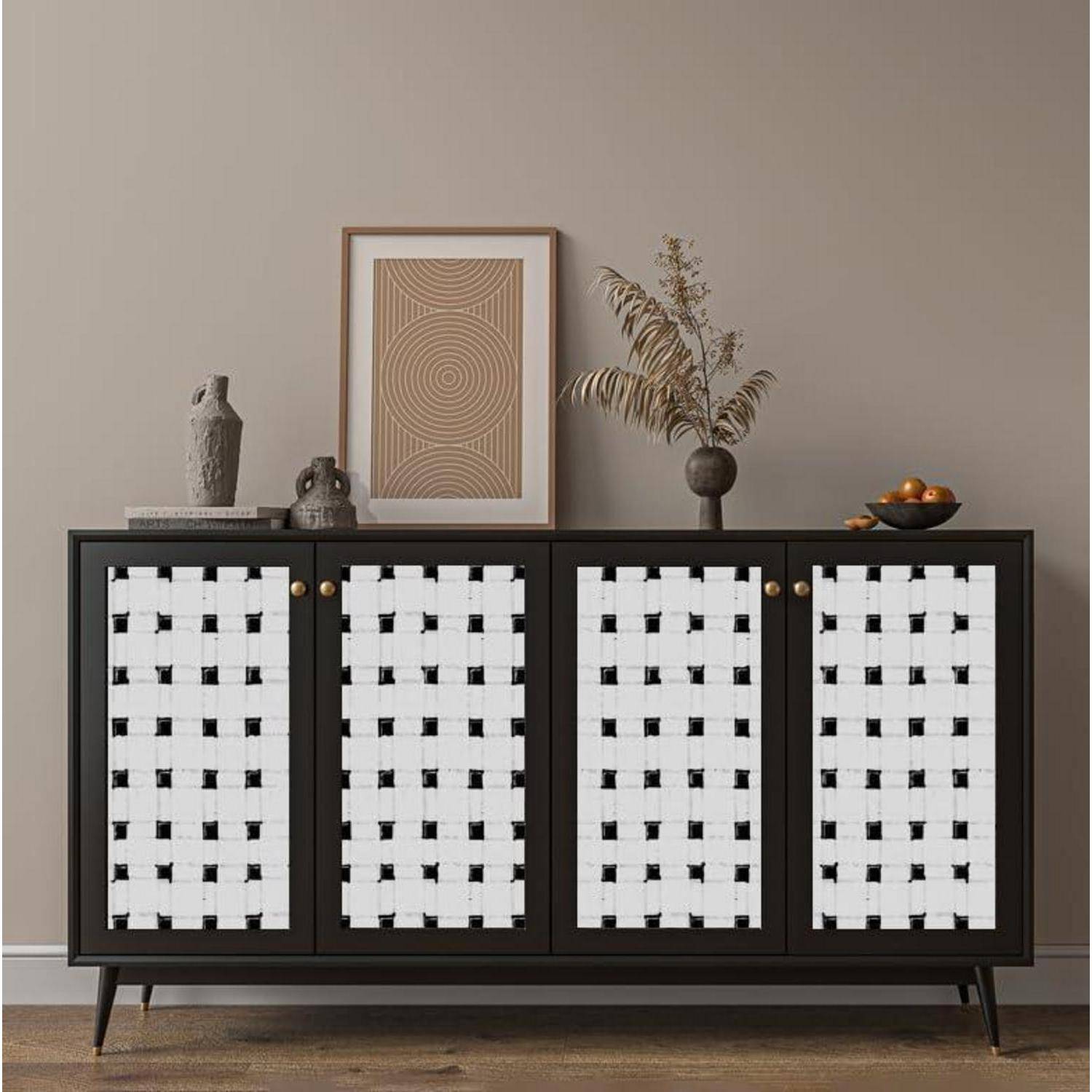 Ein schwarzes Sideboard mit gemusterten weißen Frontpaneelen ist geschmückt mit einem gerahmten geometrischen Kunstwerk, einer Keramakskulptur und einer Vase mit getrockneten Pflanzen.
