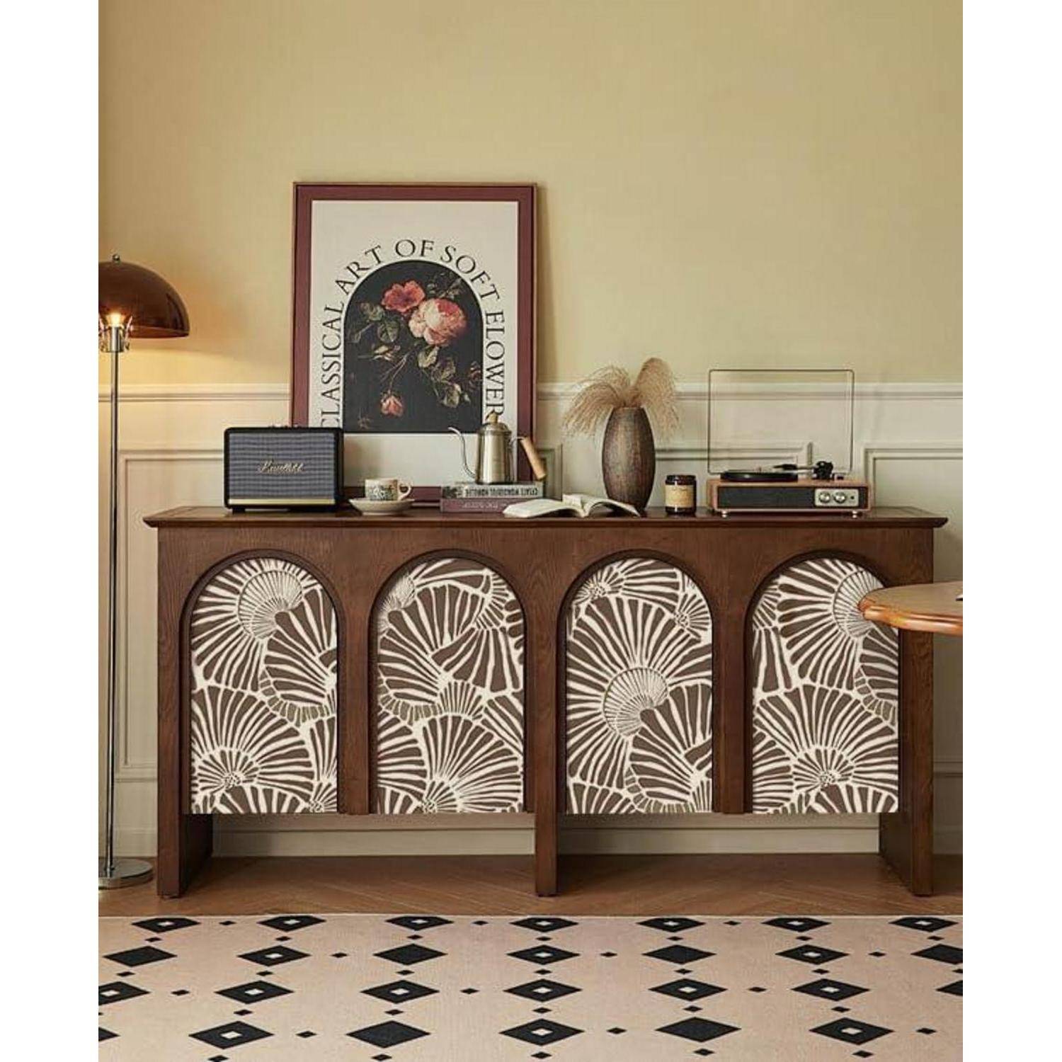 Ein Wohnzimmerensemble mit einem dekorativen Holzsideboard, das florale Muster aufweist, einen gerahmten Druck und verschiedene Gegenstände zeigt, darunter ein Radio und eine Lampe.