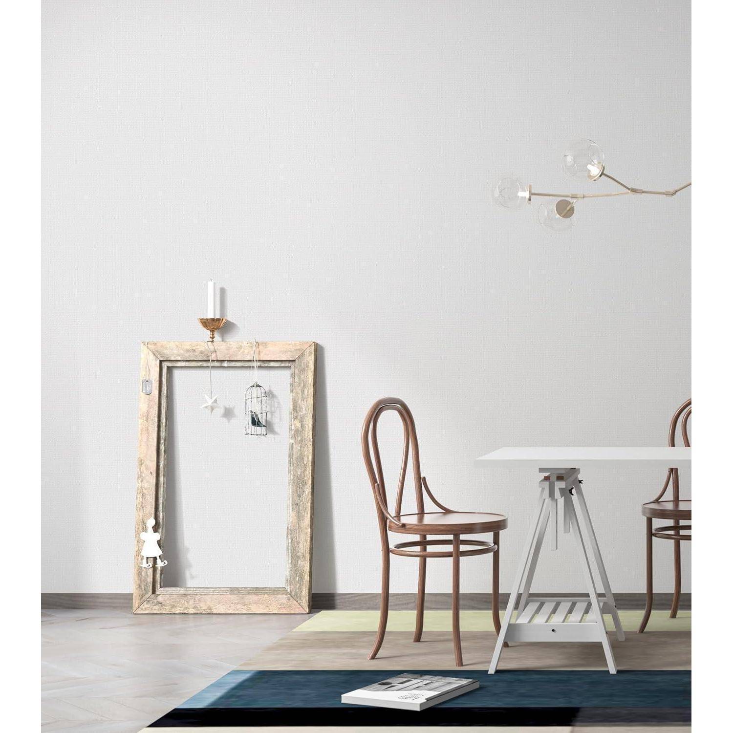 Ein minimalistisches Zimmer zeigt einen großen, lehnenden Spiegel mit Dekorationselementen, zwei Holzstühle neben einem weißen Tisch und eine moderne, verzweigte Lichtinstallation.