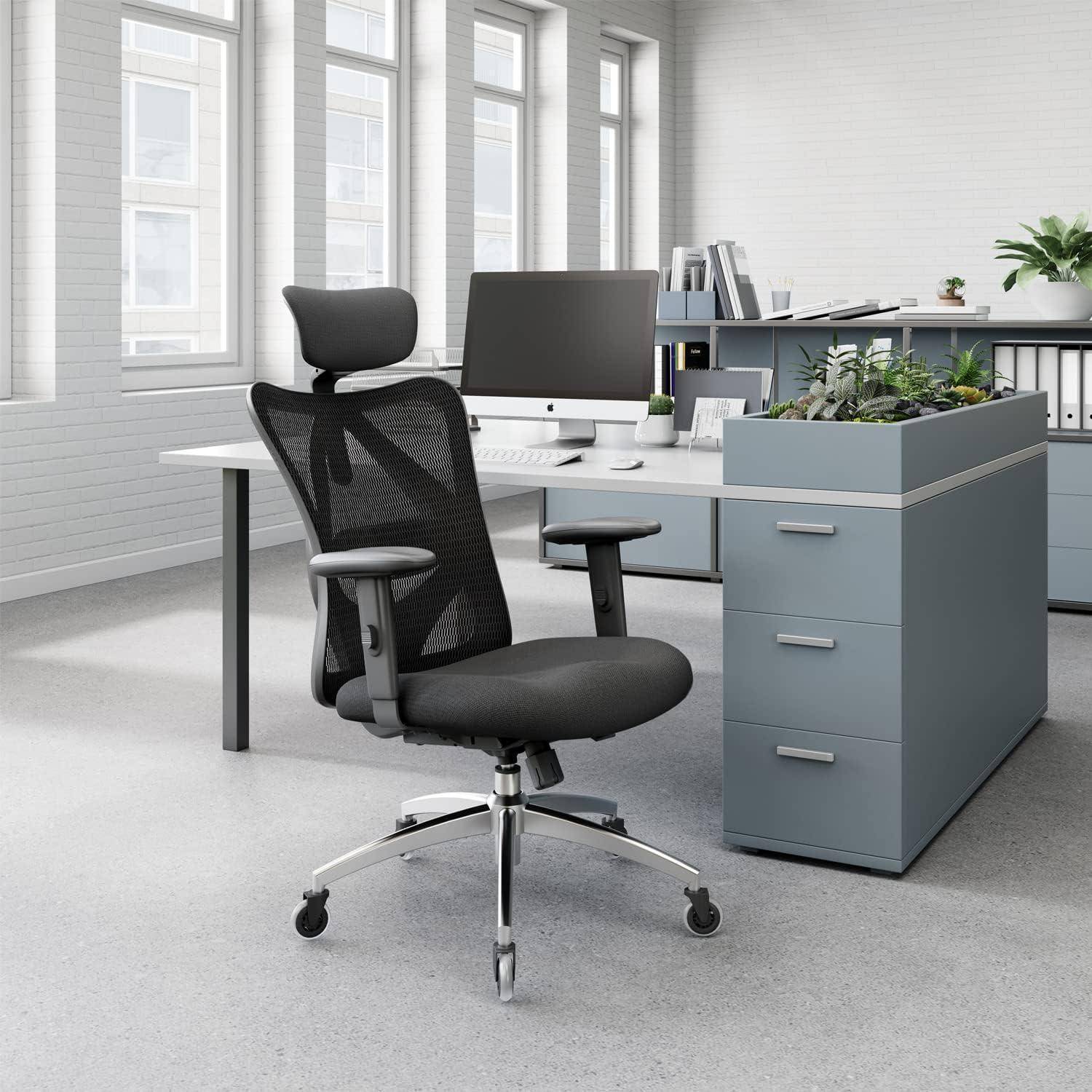 Moderner Büroraum mit einem Netzstuhl, elegantem Schreibtisch, Computer und Zimmerpflanzen auf einem Schrank, unter natürlichem Licht von großen Fenstern.