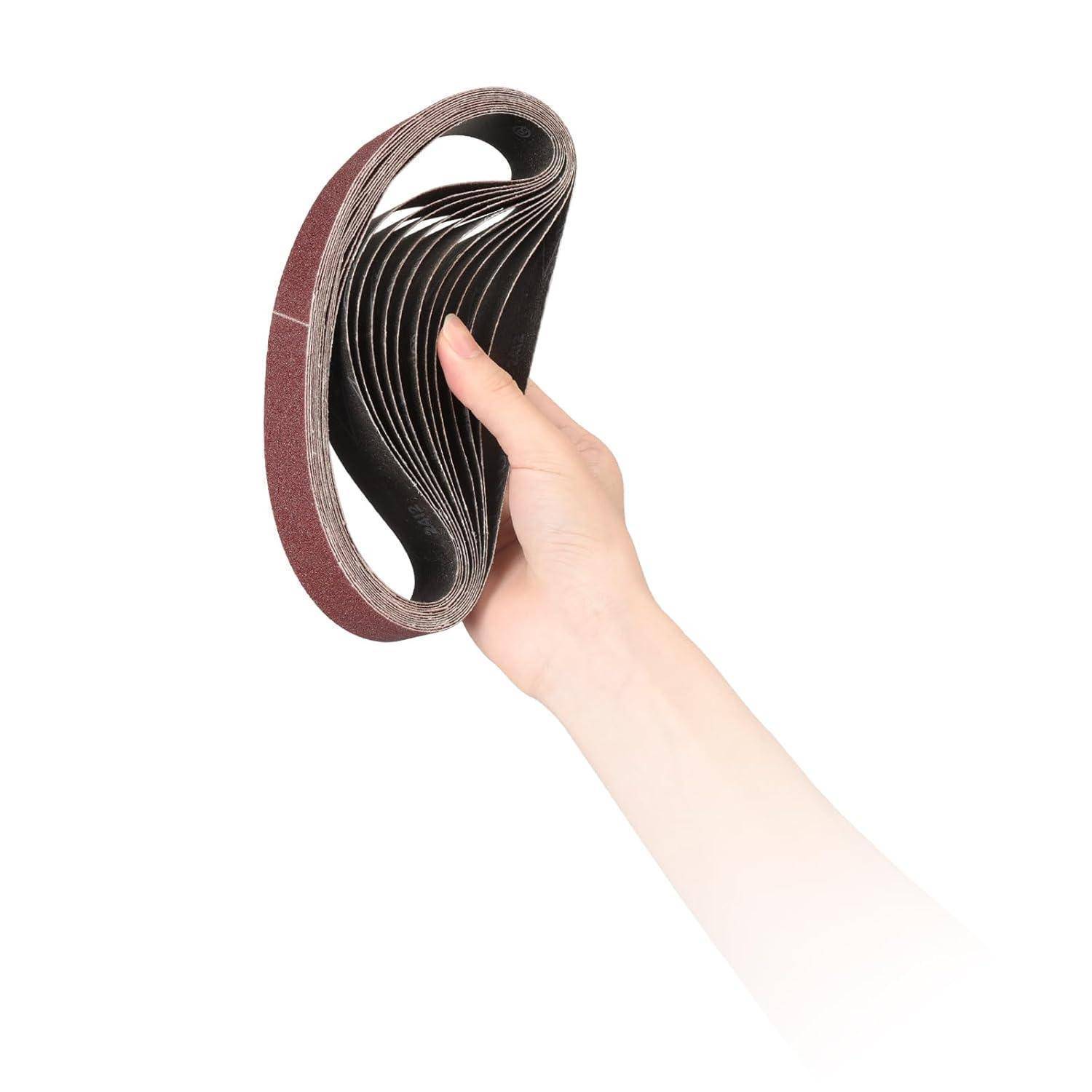 Eine Hand hält einen Stapel brauner Schleifbänder, die gefächert sind, um die geschichteten, strukturierten Oberflächen vor einem schlichten weißen Hintergrund zu zeigen.