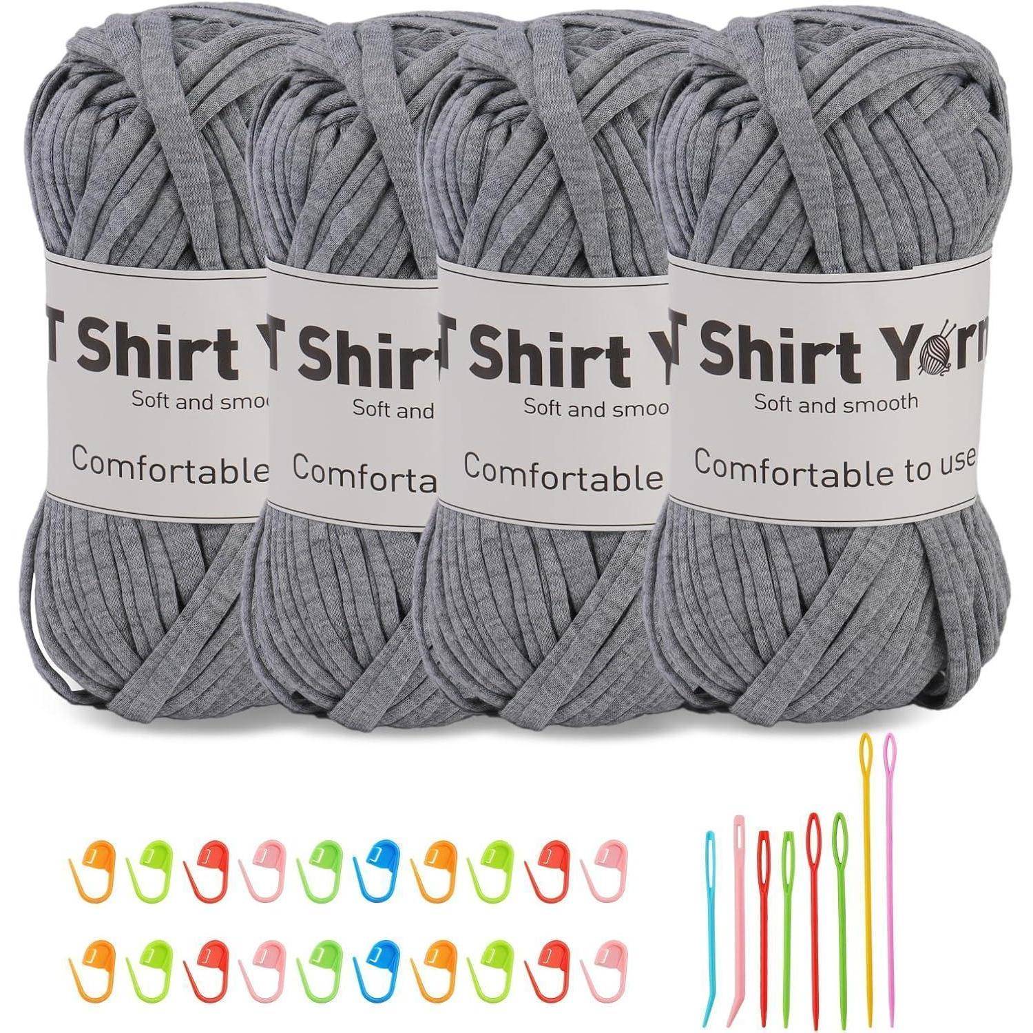 Vier Knäuel graues T-Shirt-Garn mit dem Text ‚Angenehm zu verwenden', begleitet von bunten Häkelnadeln und Maschenmarkern.
