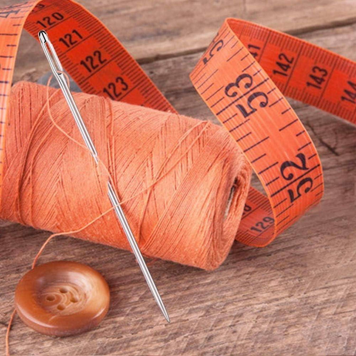 Eine Spule orangefarbenen Fadens, eine Nadel, ein Holzknopf und ein orangefarbenes Maßband auf einer Holzoberfläche, was auf Nähen oder Schneiderhandwerk hindeutet.