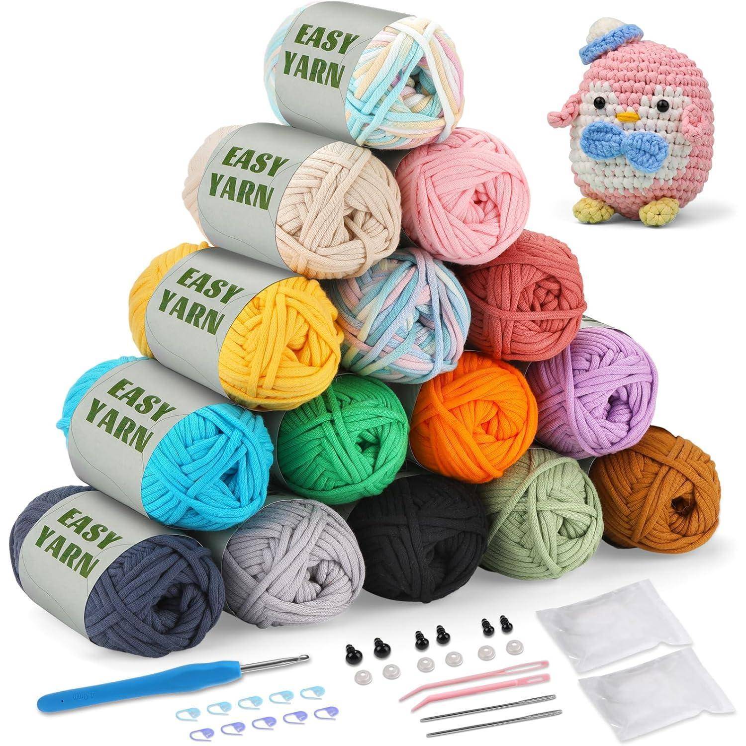 Eine Pyramide aus mehrfarbigen 'Easy Yarn' Bällen neben einer gehäkelten rosa-blauen Eule. Darunter Häkelnadeln, Stricknadeln und Maschenmarkierer.
