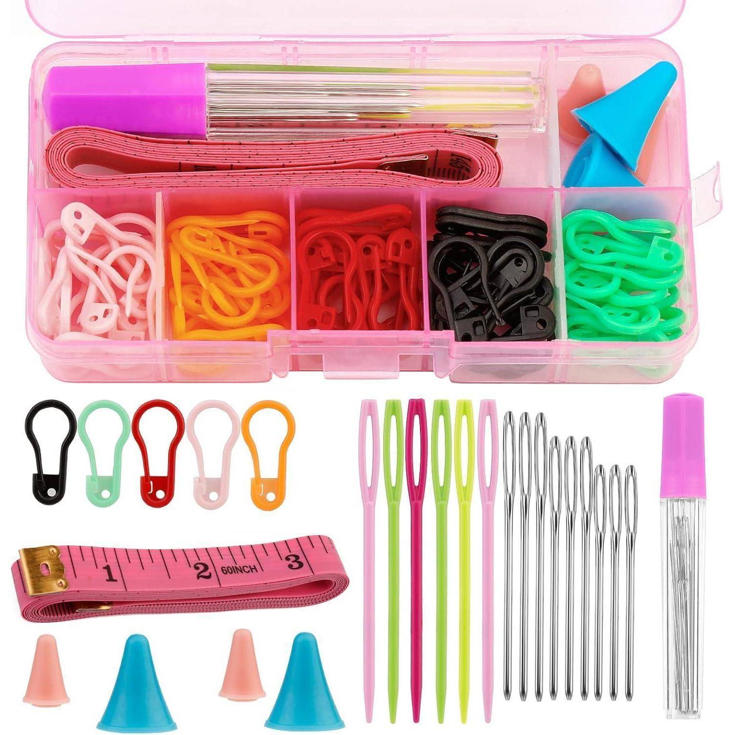 Nähset mit verschiedenen Werkzeugen in einer pinken Schachtel, einschließlich Maßband, bunten Maschenmarkierern, Nähnadeln und Fingerhüten.