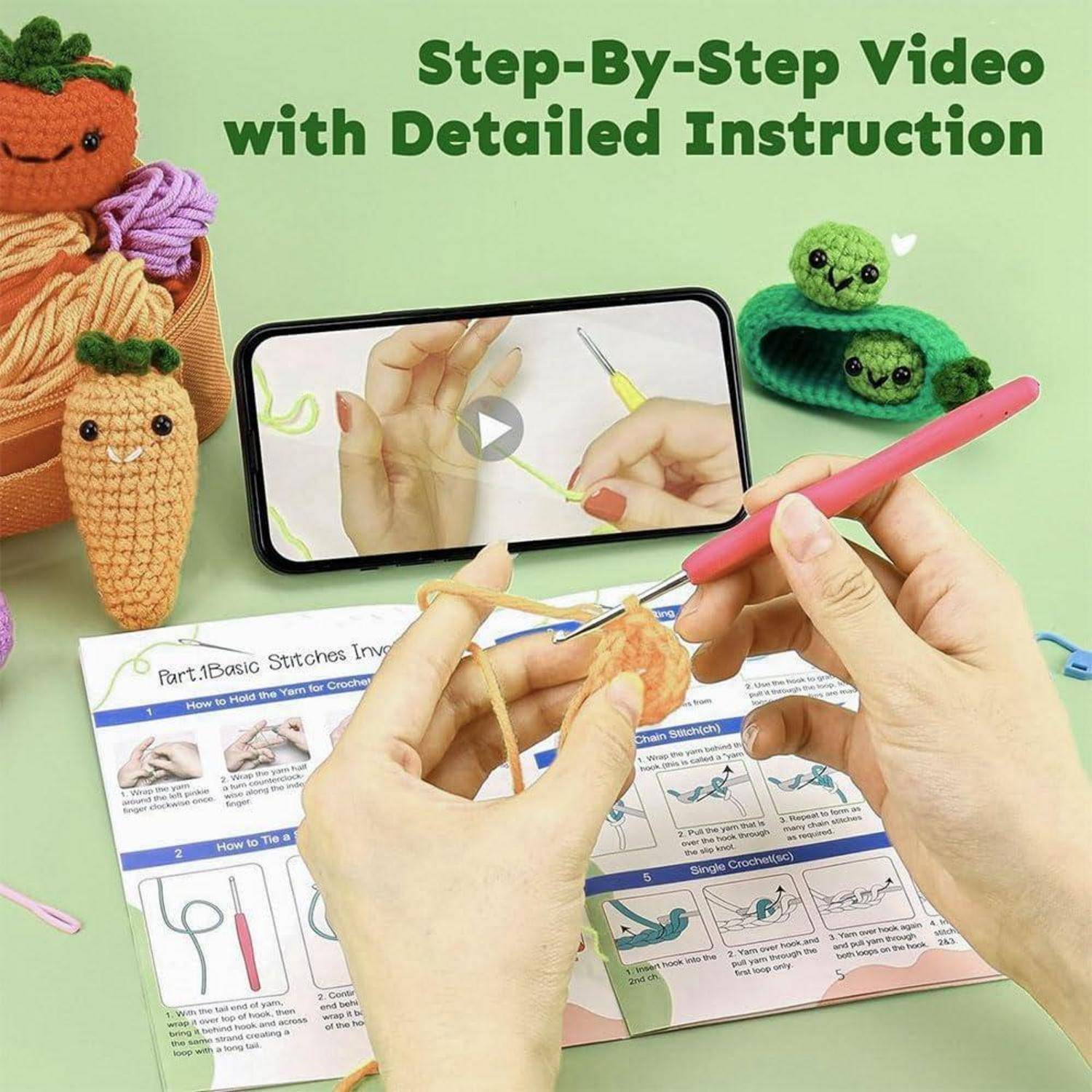 Person häkelt eine Karotte mit einer pinken Häkelnadel, während sie ein 'Schritt-für-Schritt-Video mit detaillierten Anweisungen' auf einem Smartphone anschaut.