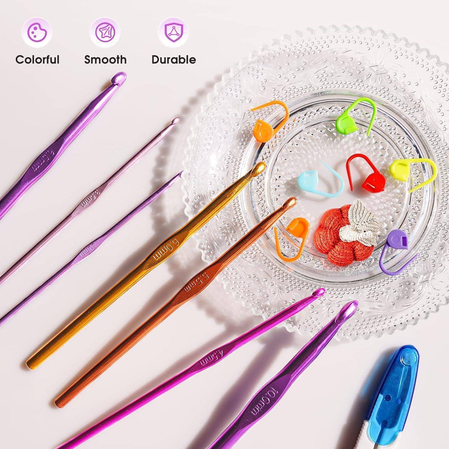 Häkelhaken in verschiedenen Farben sind neben einem Glasteller angeordnet, der Maschenmarkierer trägt. Text darüber besagt: 'Farbenfroh', 'Glatt', 'Langlebig'.