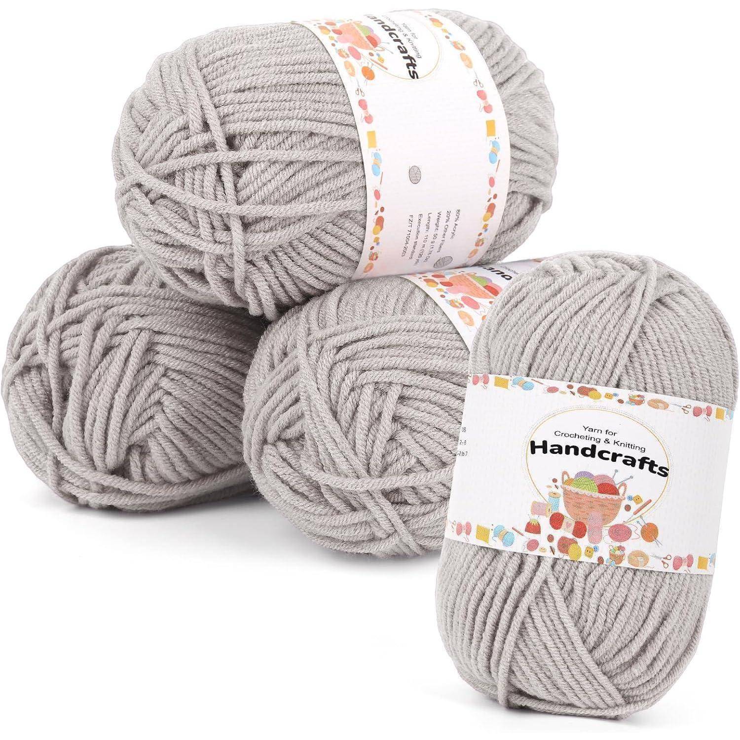 Vier Stränge grauen Garns mit der Beschriftung 'Handcrafts', in einem kleinen Häufchen angeordnet, wobei zwei Etiketten mit dekorativen Mustern sichtbar sind.