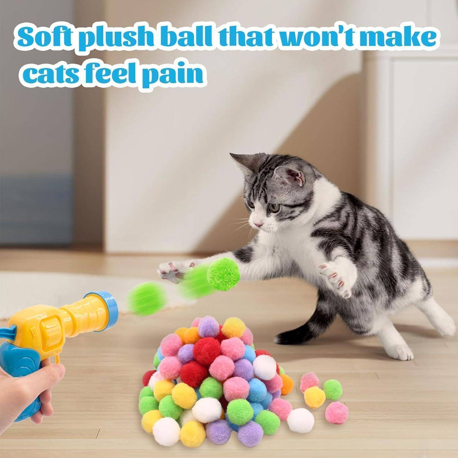 Eine verspielt Katze schlägt nach bunten, weichen Plüschbällen, während eine Hand einen Spielzeug-Launcher hält. Text liest sich: 'Weicher Plüschball, der Katzen keinen Schmerz zufügt'.