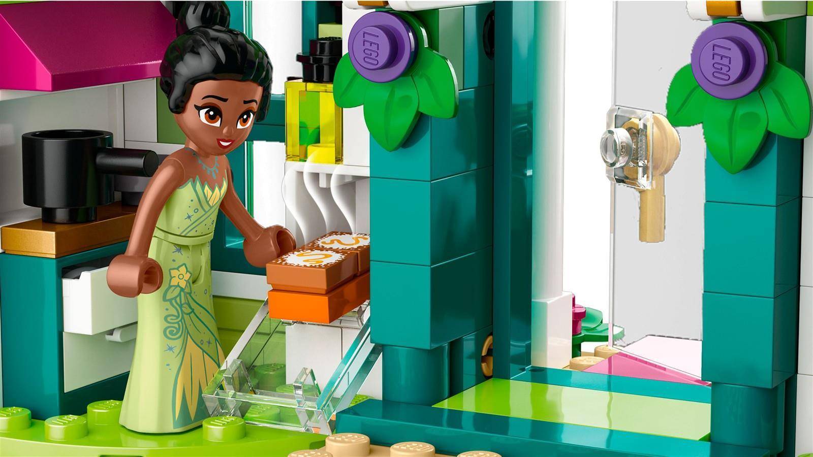 Eine LEGO-ähnliche Szene einer Frau in einem grünen Kleid, die Lebensmittel auf einer Küchentheke neben einem Kühlschrank und einer Tür ablegt oder entnimmt.