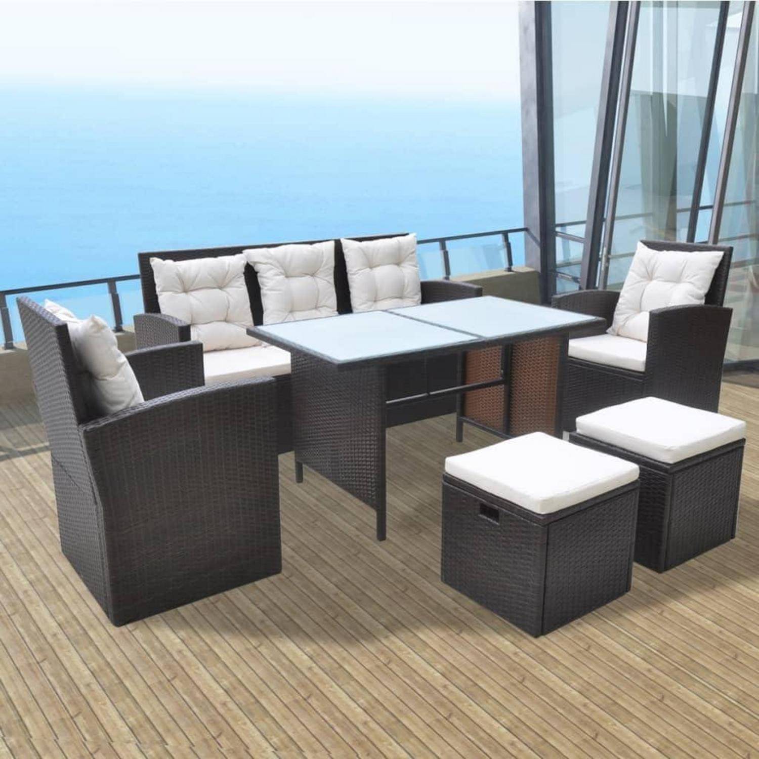 Outdoor-Terrassenmöbel mit gepolsterten Rattanstühlen und einem Glastisch auf einer Holzterrasse mit Blick auf den Ozean und großen Fenstern.