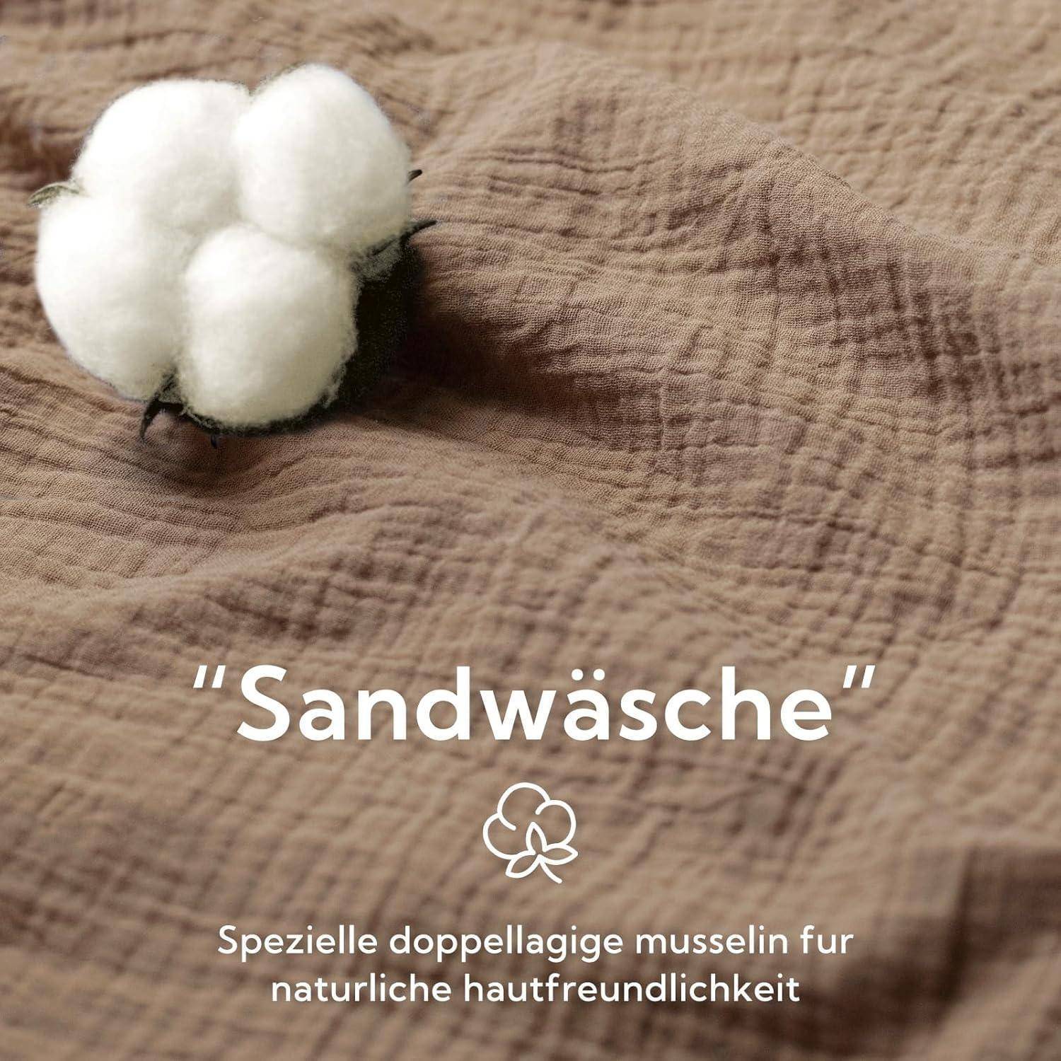 Eine Baumwollkapsel auf strukturiertem braunem Stoff mit dem Text: ‚Sandwäsche', was eine spezielle zweischichtige Musselin-Qualität für natürliche Hautfreundlichkeit bedeutet.