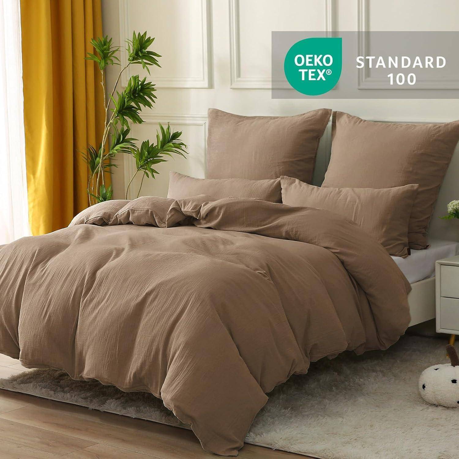 Ein sauber gemachtes Bett mit brauner Bettwäsche steht in einem hellen Raum, der mit grünen Pflanzen geschmückt ist. Ein 'OEKO-TEX STANDARD 100' Etikett ist sichtbar.