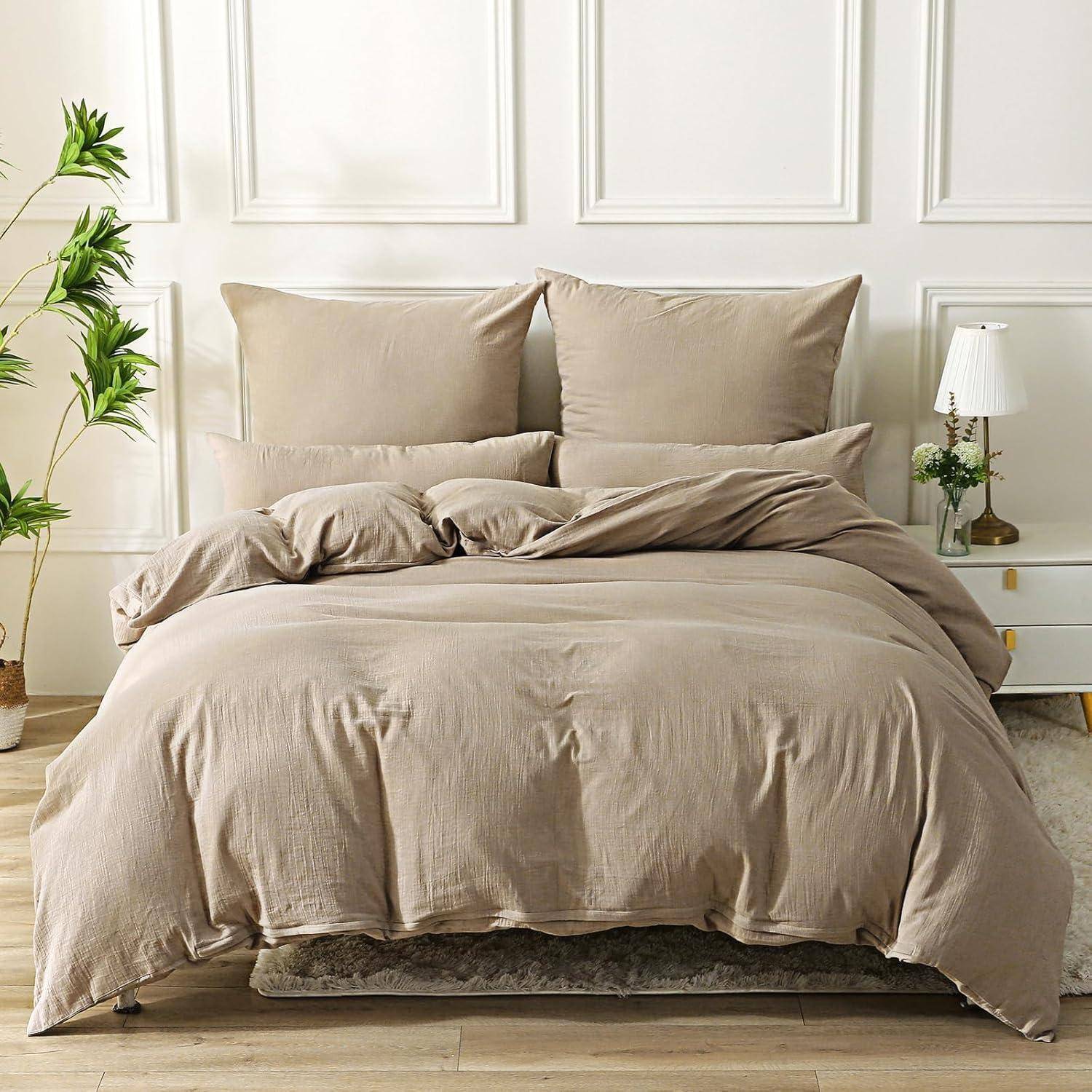 Ein ordentlich gemachtes Bett mit beigefarbener Bettwäsche, Kissen und einem Bettdecken in einem Raum mit einer Zimmerpflanze und einem kleinen Nachttisch mit einer Lampe.