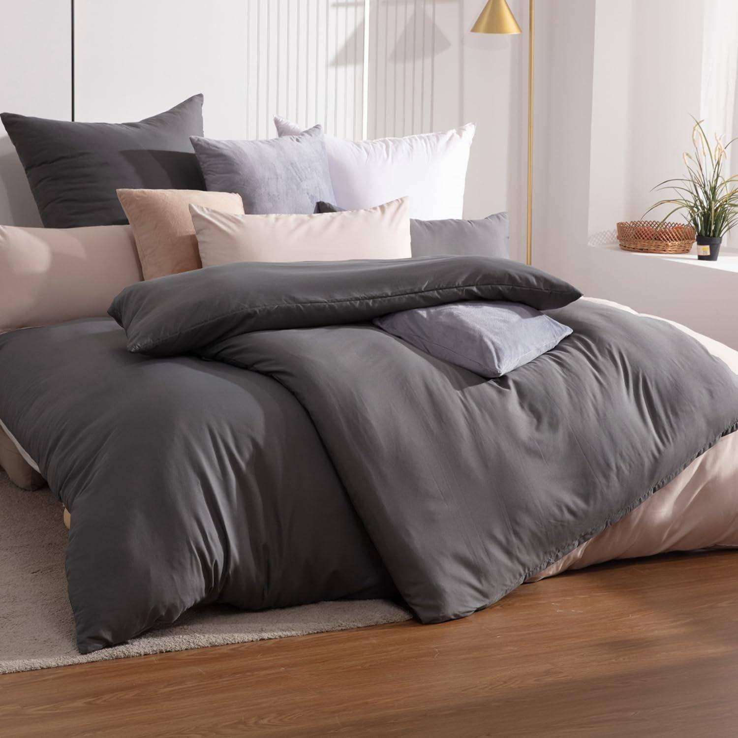 Ein sorgfältig gemachtes Bett mit grauer Bettwäsche und mehreren Kissen in einem modernen Schlafzimmer mit hellem Holzboden und einer kleinen Pflanze auf einem Tisch.