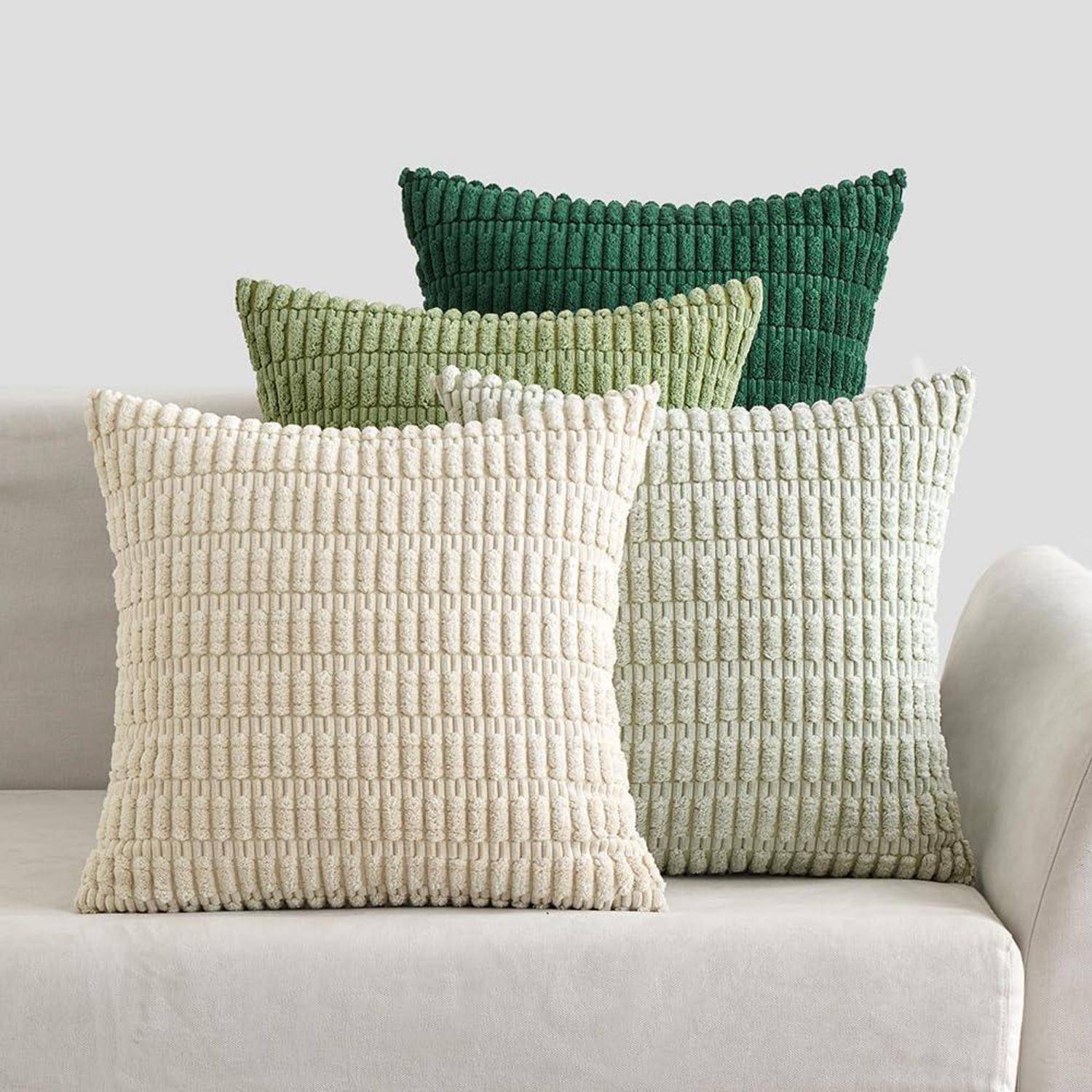 Drei strukturierte Kissen in verschiedenen Schattierungen von Grün und Beige sind auf einem hellgefärbten Sofa vor einem einfarbigen Hintergrund angeordnet.